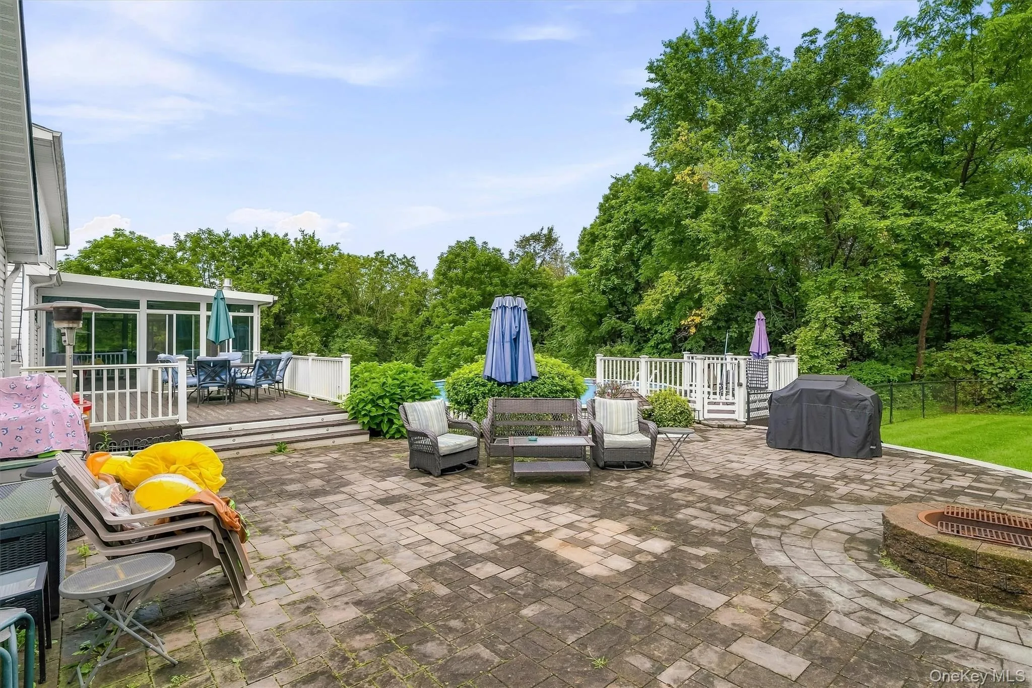 Expansive paver patio with a built-in fire pit, leading to a raised deck with a sunroom addition Expansive paver patio with a built-in fire pit, leading to a raised deck with a sunroom addition