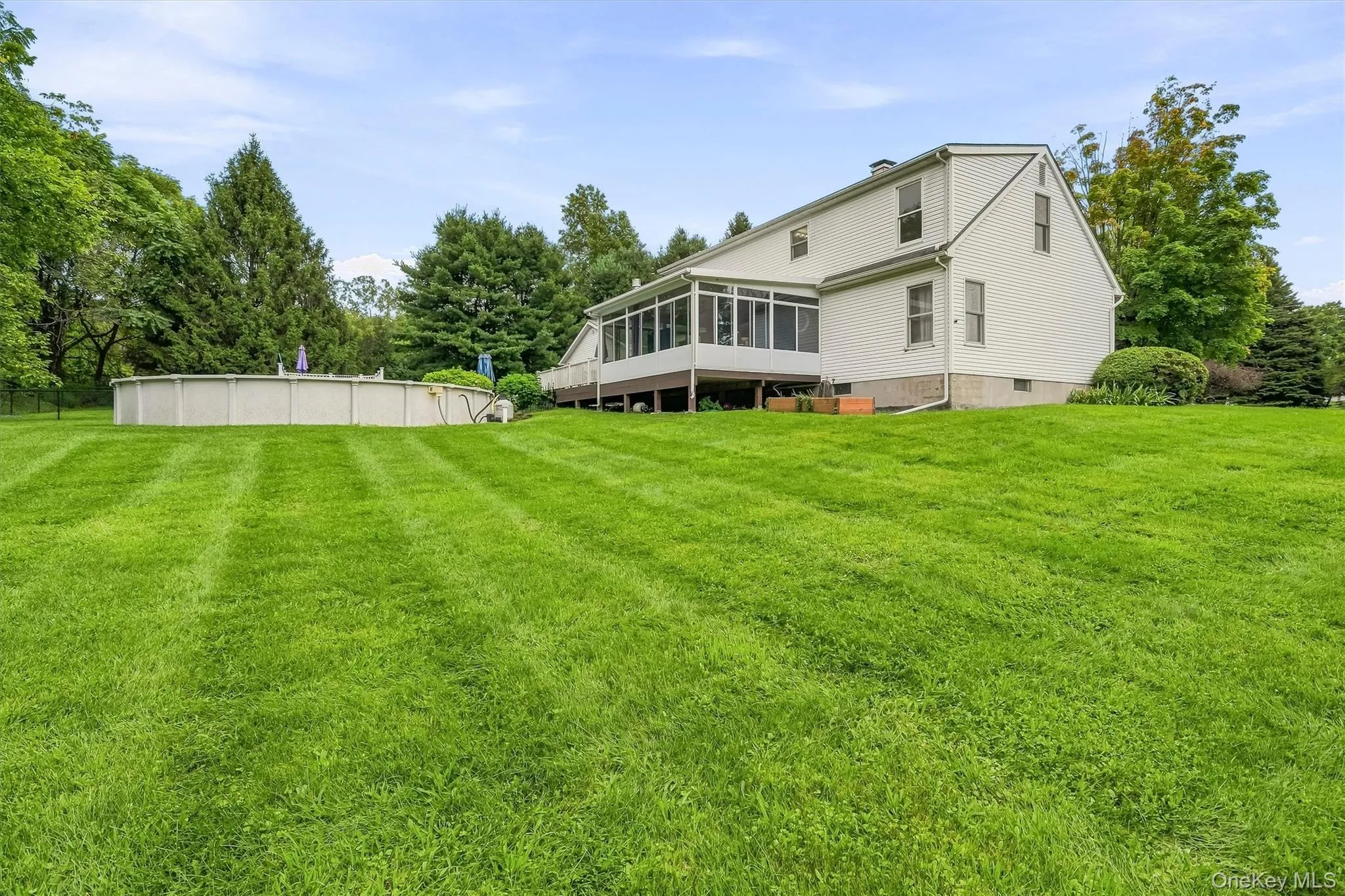 Expansive lawn with an above-ground pool, a screened-in porch, and a white-sided exterior Expansive lawn with an above-ground pool, a screened-in porch, and a white-sided exterior