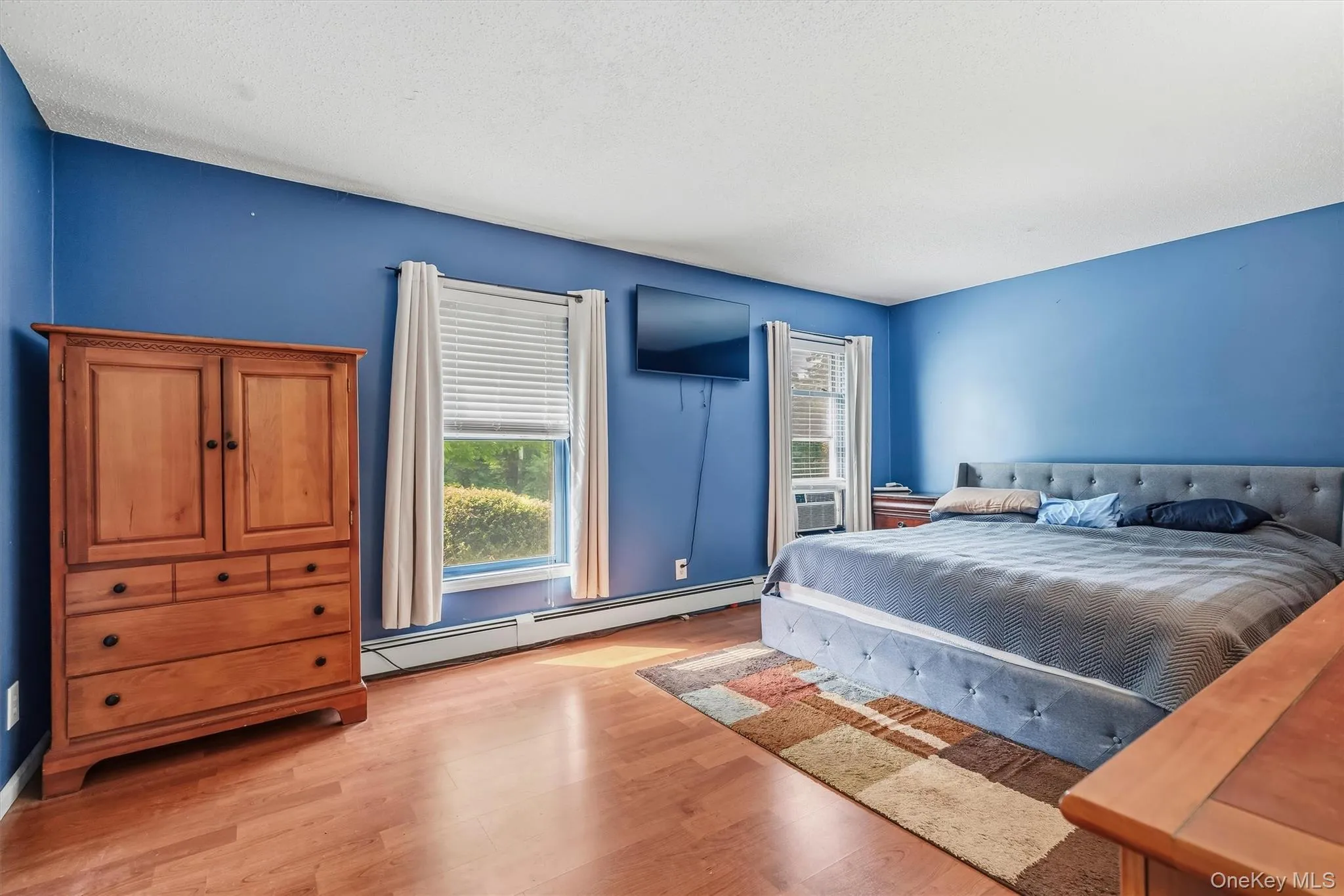 Spacious primary bedroom with hardwood flooring and multiple windows providing natural light. Spacious primary bedroom with hardwood flooring and multiple windows providing natural light.