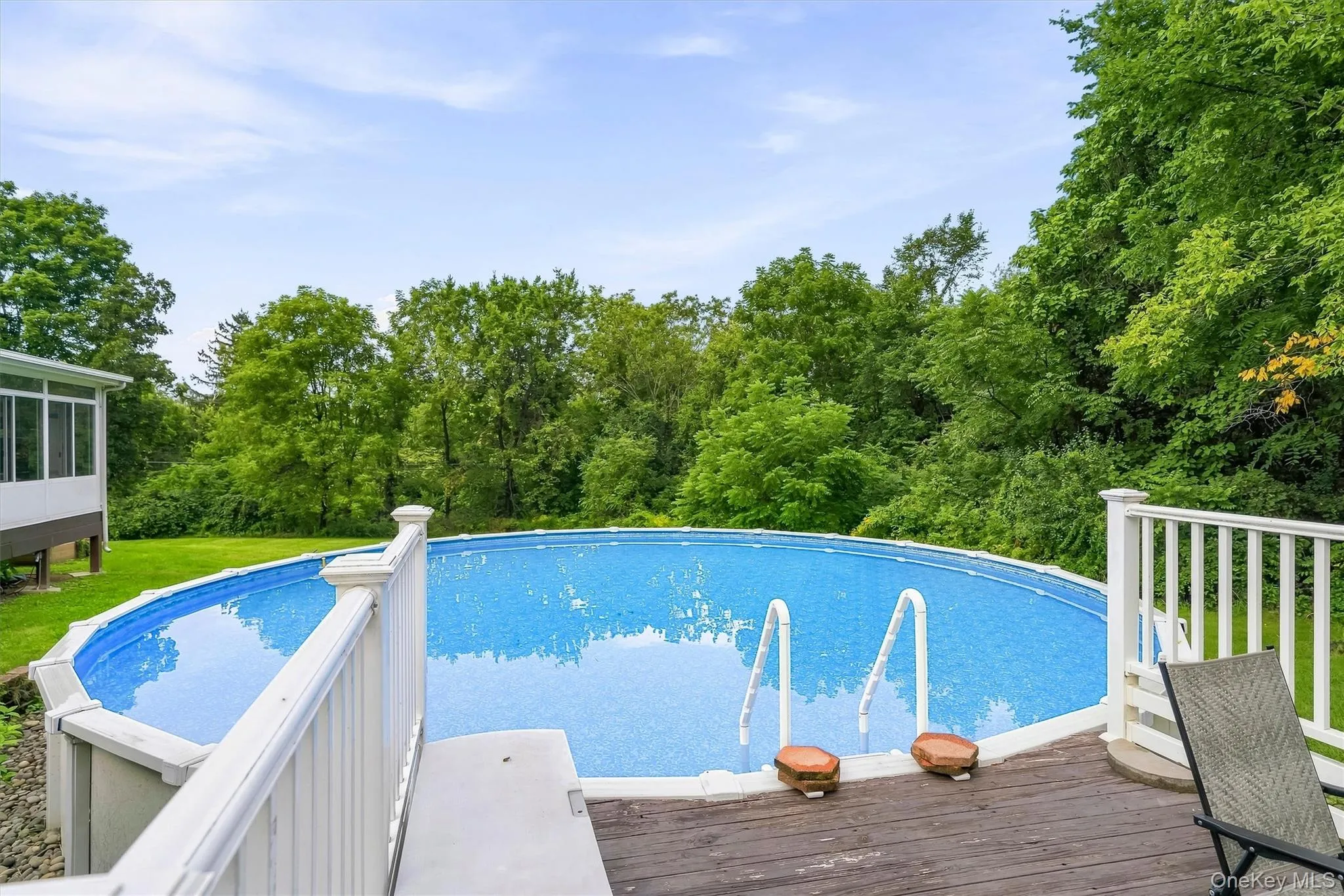 Expansive backyard featuring an above-ground pool with integrated deck access, white railing, and lush perimeter greenery Expansive backyard featuring an above-ground pool with integrated deck access, white railing, and lush perimeter greenery