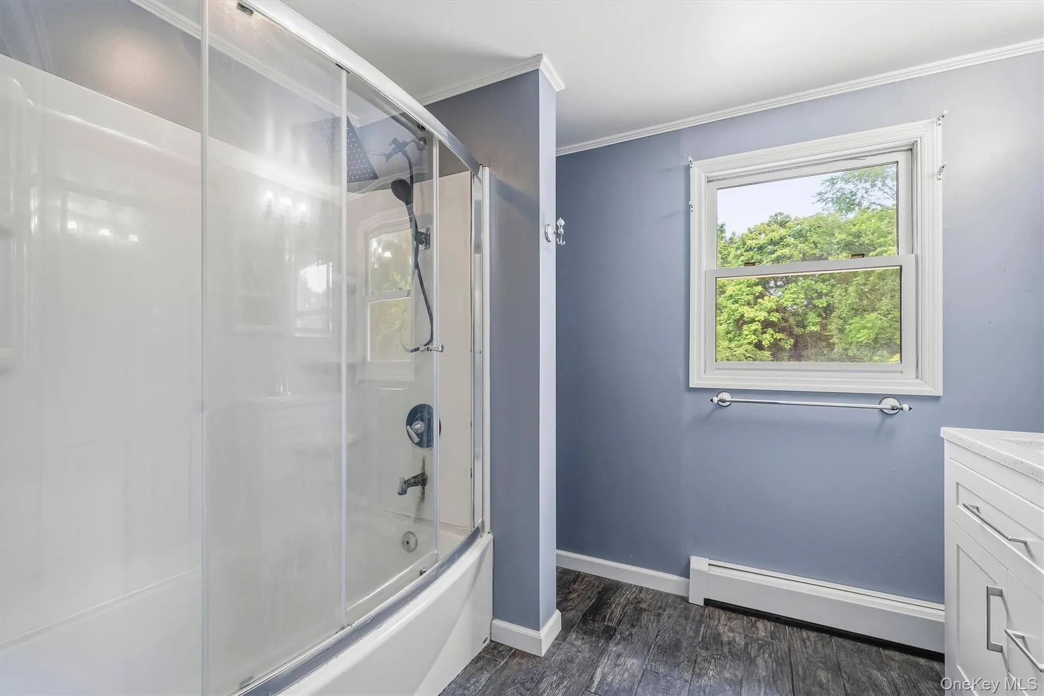 Bathtub with glass sliding doors and an integrated shower system, a single-hung window, chrome fixtures, and wood-finish flooring Bathtub with glass sliding doors and an integrated shower system, a single-hung window, chrome fixtures, and wood-finish flooring