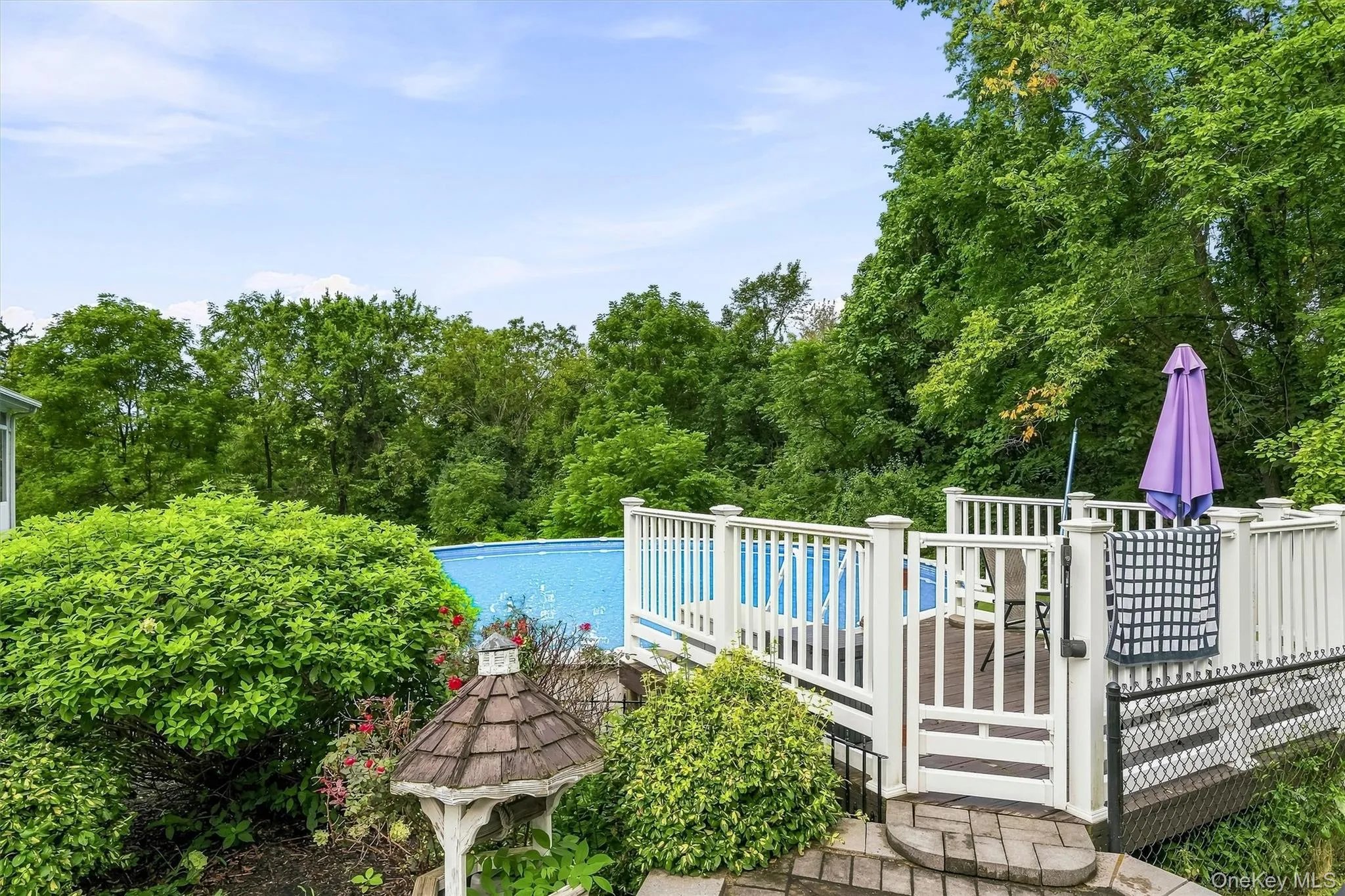Raised deck with white railings and gate, featuring an above-ground pool, surrounded by mature trees Raised deck with white railings and gate, featuring an above-ground pool, surrounded by mature trees