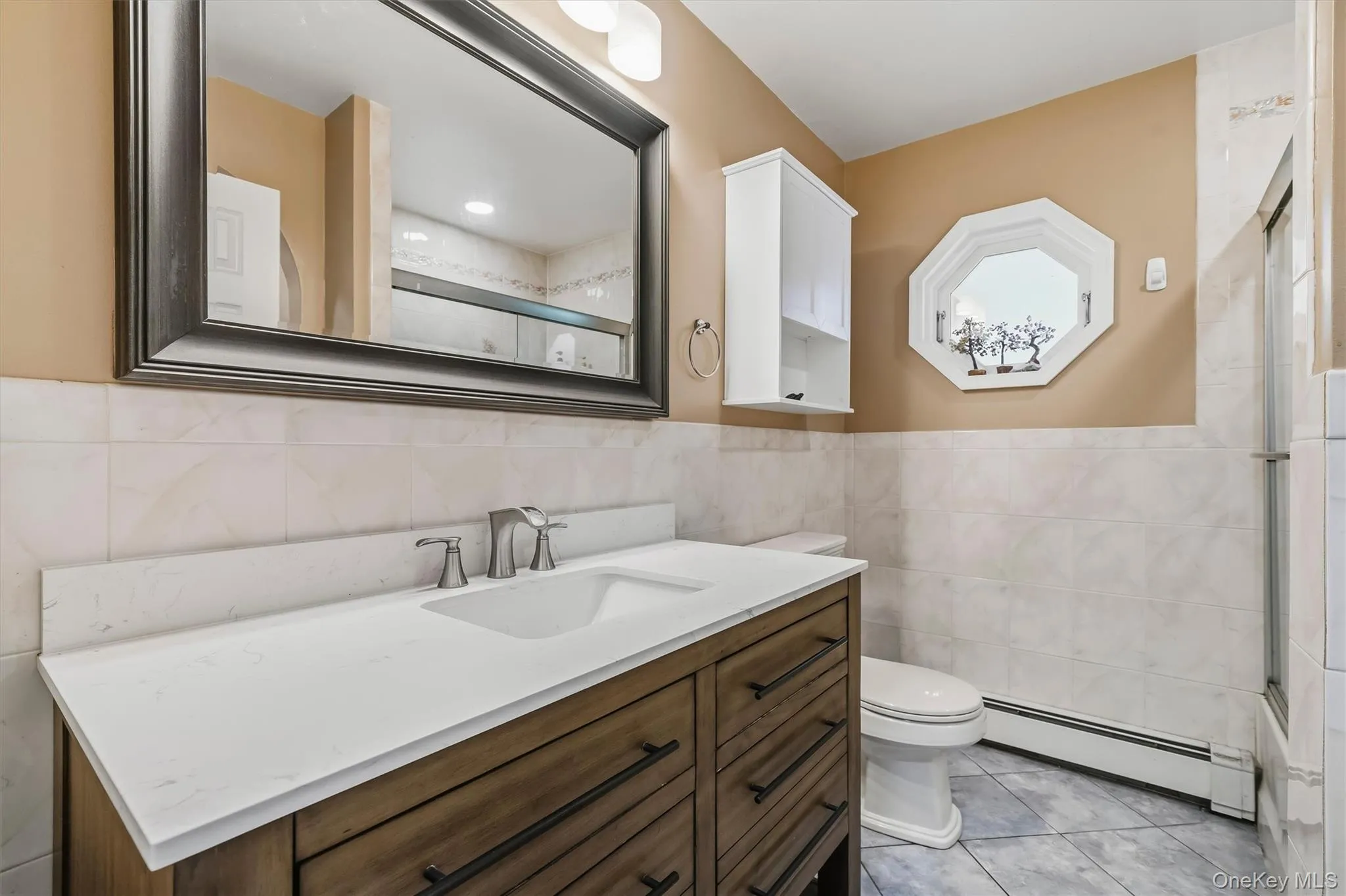 Vanity with integrated sink and chrome faucet, rectangular framed mirror, octagonal window, half-wall tile surround, and built-in wall cabinet Vanity with integrated sink and chrome faucet, rectangular framed mirror, octagonal window, half-wall tile surround, and built-in wall cabinet