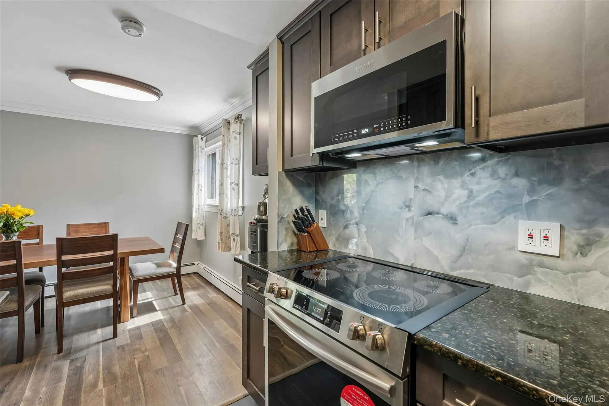 Stainless steel electric range, dark granite-style countertop, full-height backsplash, wood-finish flooring, and dark wood-finish cabinetry Stainless steel electric range, dark granite-style countertop, full-height backsplash, wood-finish flooring, and dark wood-finish cabinetry