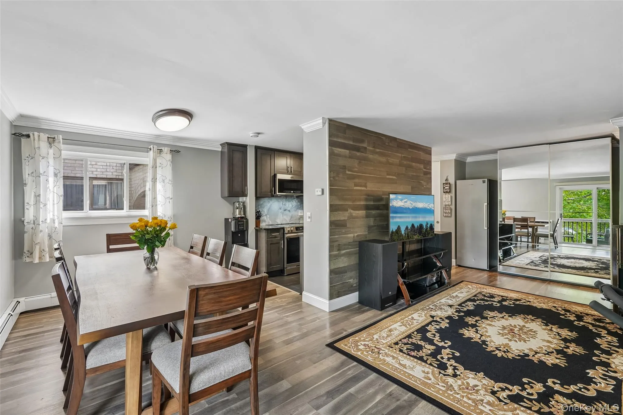 Open-concept living space with wood-finish flooring, a dining area, and a kitchen featuring dark wood cabinetry Open-concept living space with wood-finish flooring, a dining area, and a kitchen featuring dark wood cabinetry