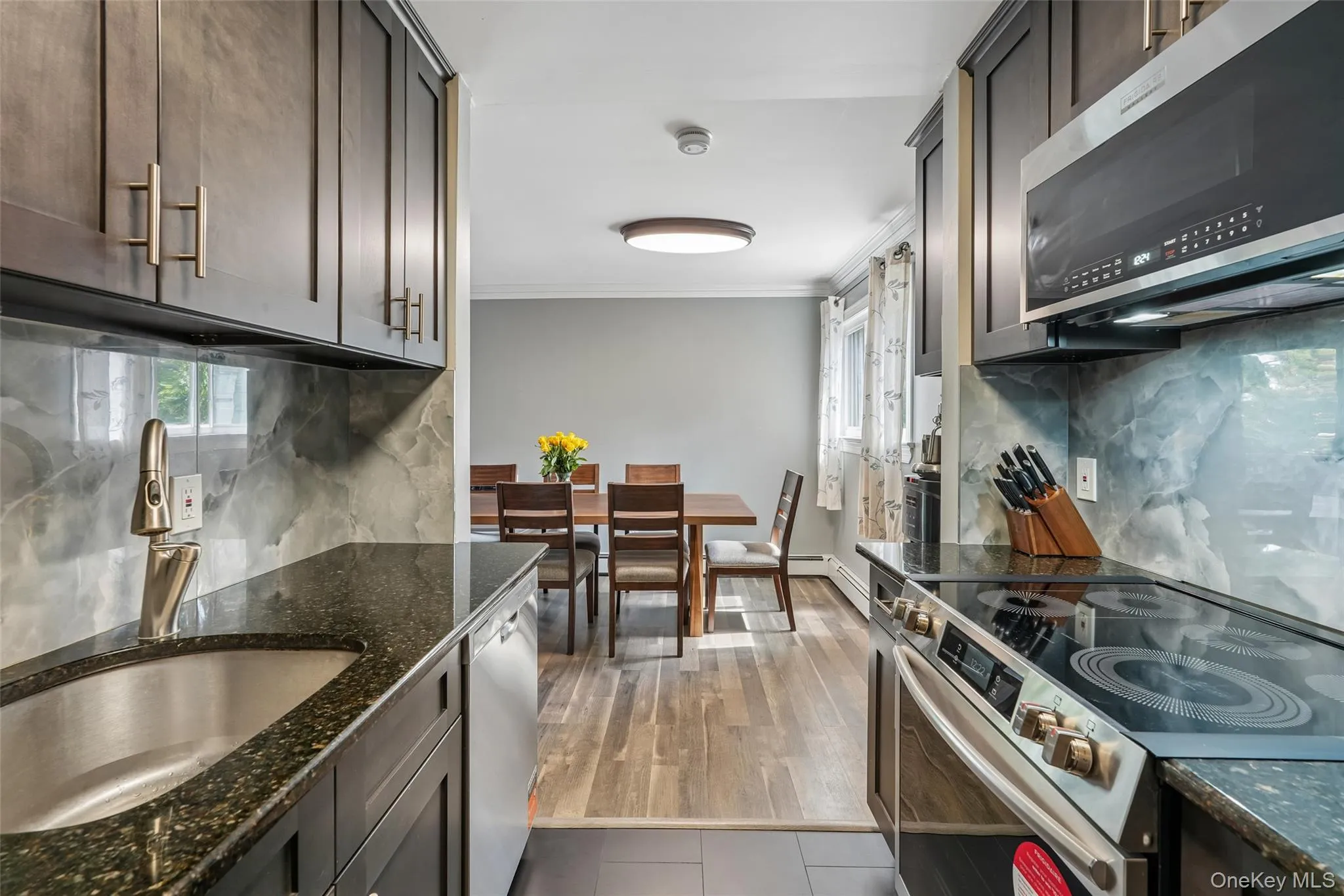 Dark wood-finish cabinetry with modern hardware, stainless steel sink with a pull-down faucet, built-in microwave, and a smooth-top electric range Dark wood-finish cabinetry with modern hardware, stainless steel sink with a pull-down faucet, built-in microwave, and a smooth-top electric range