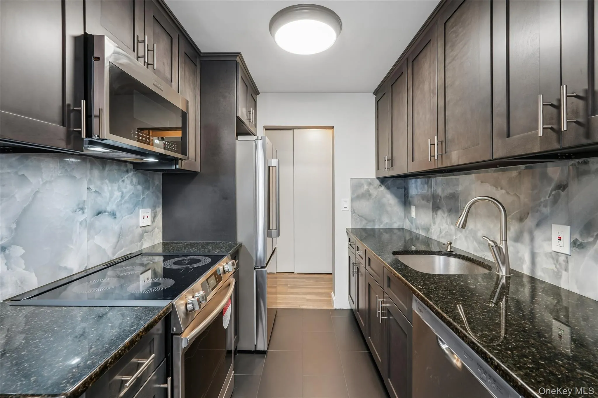 Galley kitchen featuring dark wood cabinetry, stainless steel appliances, a black electric cooktop, and a stainless steel sink with a high-arc faucet Galley kitchen featuring dark wood cabinetry, stainless steel appliances, a black electric cooktop, and a stainless steel sink with a high-arc faucet