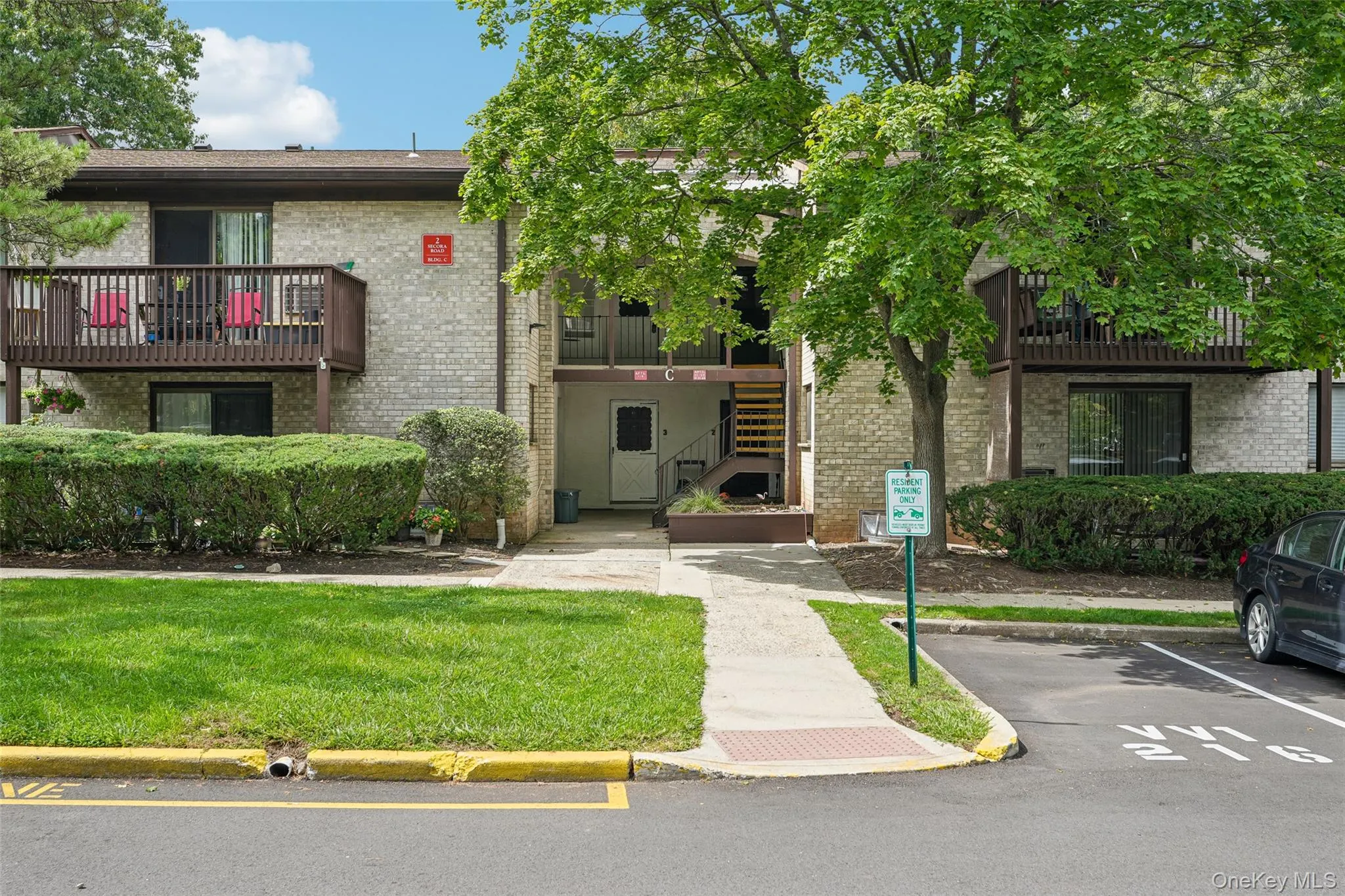 Brick exterior with private balcony, surrounding green landscaping, and paved parking area Brick exterior with private balcony, surrounding green landscaping, and paved parking area