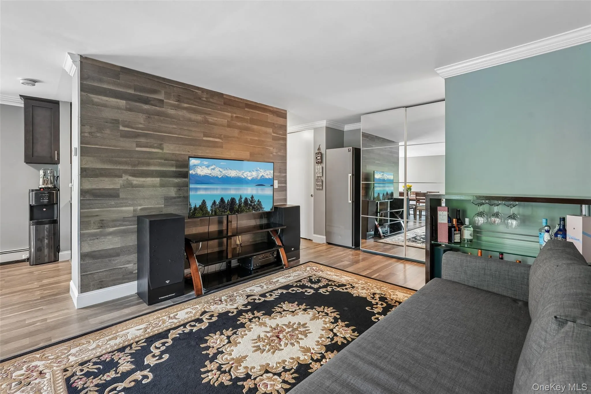Hardwood-style flooring throughout, accent wall with horizontal wood paneling, mirrored closet doors, and a built-in bar with glass shelving Hardwood-style flooring throughout, accent wall with horizontal wood paneling, mirrored closet doors, and a built-in bar with glass shelving