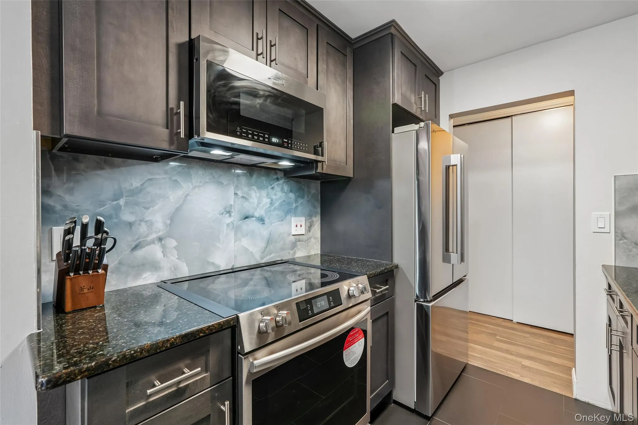 Dark wood-finish cabinetry with silver hardware, stone countertops, a glass cooktop, and stainless steel appliances Dark wood-finish cabinetry with silver hardware, stone countertops, a glass cooktop, and stainless steel appliances