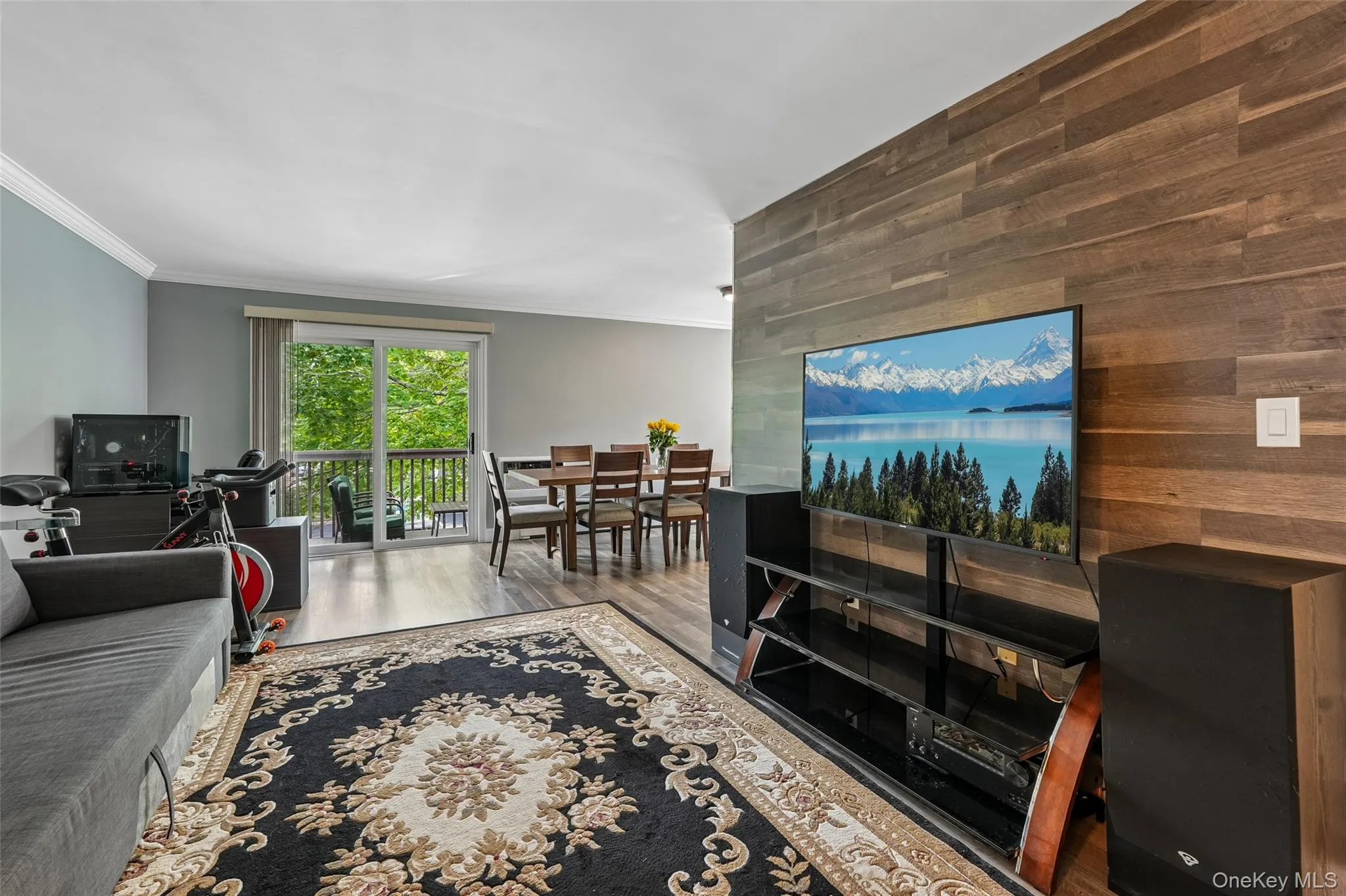 Open living area with wood-finish flooring, a wood-paneled accent wall, and crown molding Open living area with wood-finish flooring, a wood-paneled accent wall, and crown molding