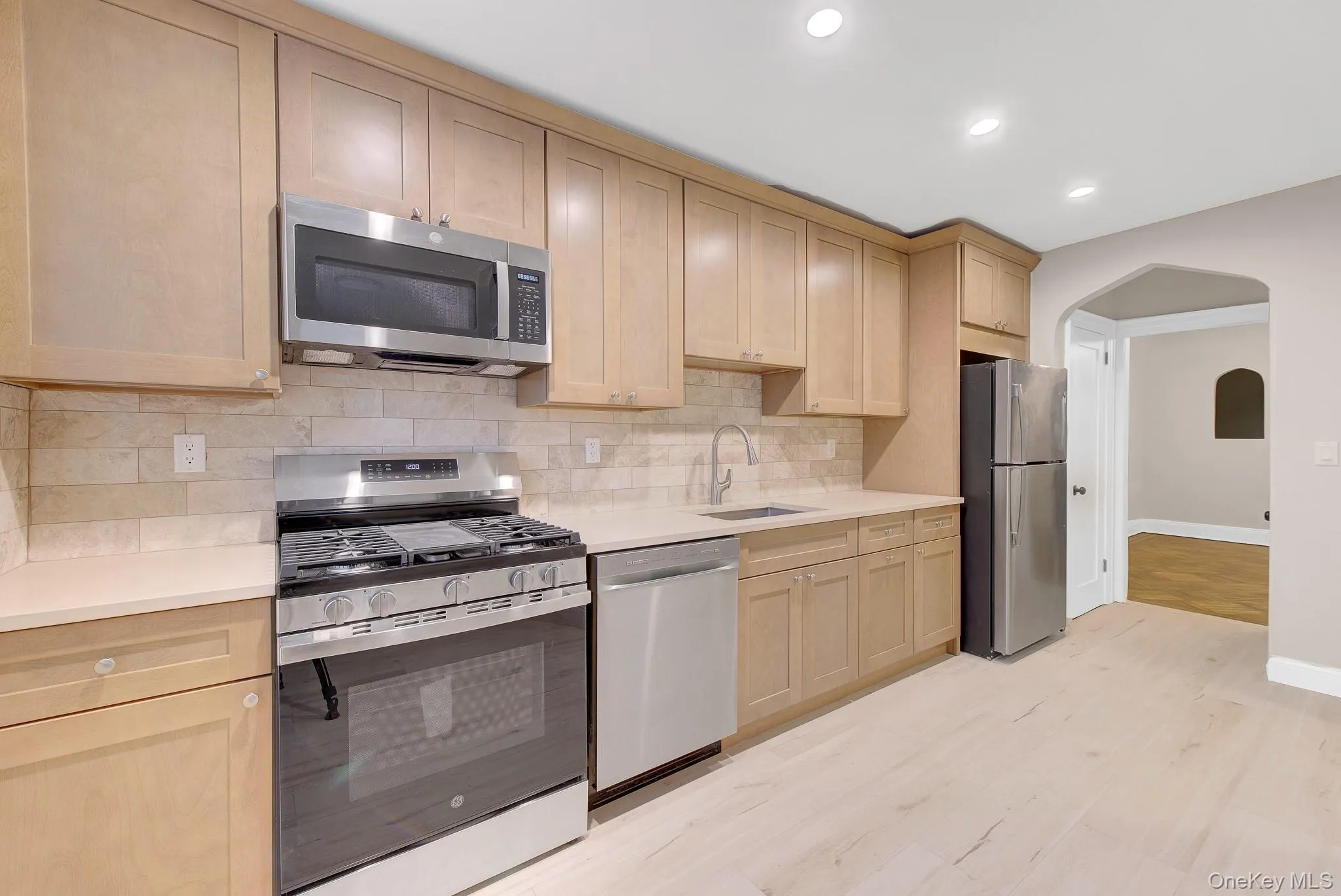 Kitchen featuring stainless steel appliances, light wood-finish cabinetry, light-toned countertops, tile backsplash, and light wood-finish flooring Kitchen featuring stainless steel appliances, light wood-finish cabinetry, light-toned countertops, tile backsplash, and light wood-finish flooring
