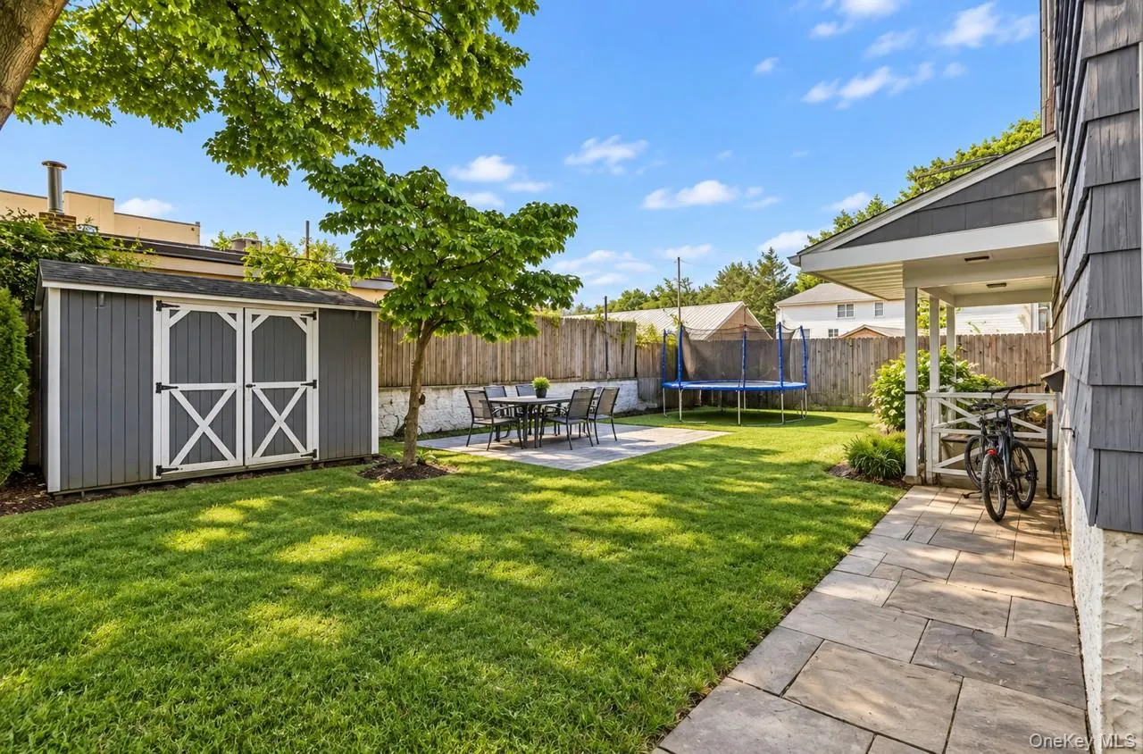 Expansive backyard featuring a manicured lawn, established trees, and a gray storage shed with white crossbuck doors Expansive backyard featuring a manicured lawn, established trees, and a gray storage shed with white crossbuck doors