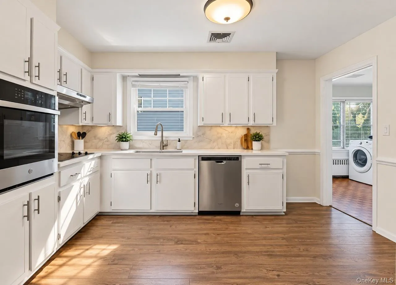 White cabinetry with modern T-bar pulls, stainless steel appliances, and wood-finish flooring White cabinetry with modern T-bar pulls, stainless steel appliances, and wood-finish flooring