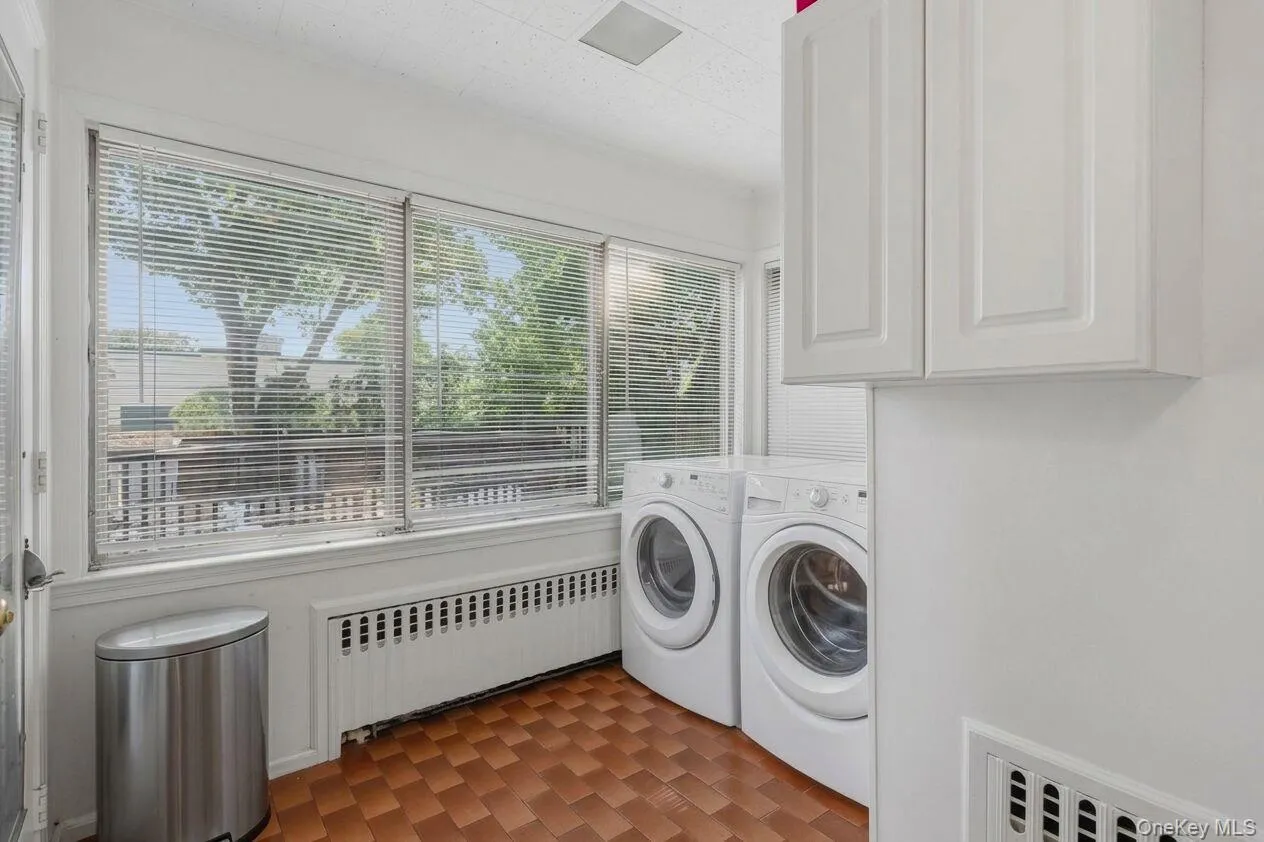 Laundry area featuring full-size washer and dryer, tile flooring, window treatments, and white overhead cabinetry Laundry area featuring full-size washer and dryer, tile flooring, window treatments, and white overhead cabinetry