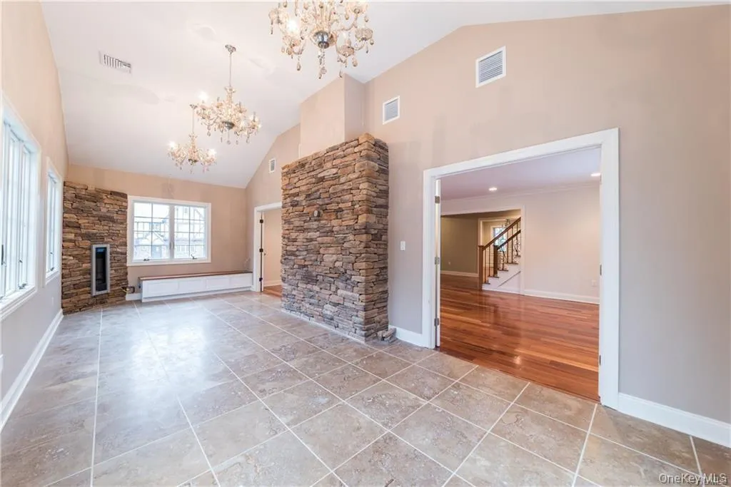 Unfurnished living room with a chandelier, high vaulted ceiling, stairway, a stone fireplace, and baseboards Unfurnished living room with a chandelier, high vaulted ceiling, stairway, a stone fireplace, and baseboards