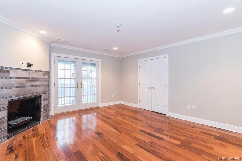 Unfurnished living room featuring french doors, wood finished floors, baseboards, ornamental molding, and a fireplace Unfurnished living room featuring french doors, wood finished floors, baseboards, ornamental molding, and a fireplace
