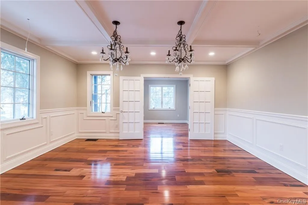Unfurnished dining area with a chandelier, beamed ceiling, a decorative wall, wood finished floors, and a wainscoted wall Unfurnished dining area with a chandelier, beamed ceiling, a decorative wall, wood finished floors, and a wainscoted wall