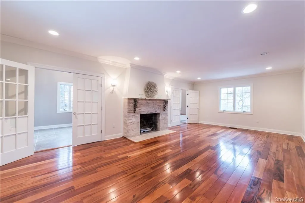 Unfurnished living room with ornamental molding, wood-type flooring, baseboards, a fireplace with flush hearth, and recessed lighting Unfurnished living room with ornamental molding, wood-type flooring, baseboards, a fireplace with flush hearth, and recessed lighting