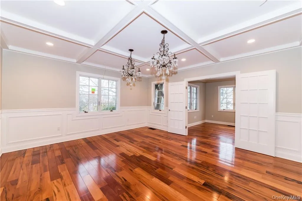 Unfurnished dining area featuring coffered ceiling, a chandelier, wood-type flooring, wainscoting, and beamed ceiling Unfurnished dining area featuring coffered ceiling, a chandelier, wood-type flooring, wainscoting, and beamed ceiling