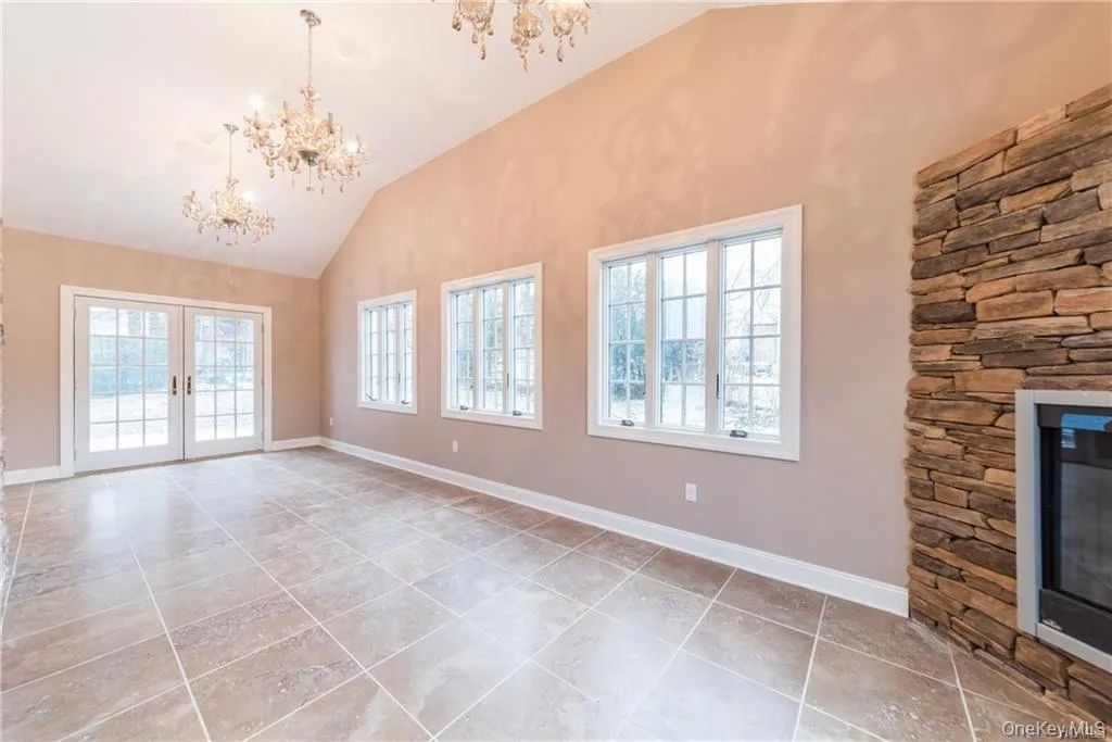 Unfurnished living room featuring a chandelier, french doors, light tile patterned floors, baseboards, and high vaulted ceiling Unfurnished living room featuring a chandelier, french doors, light tile patterned floors, baseboards, and high vaulted ceiling