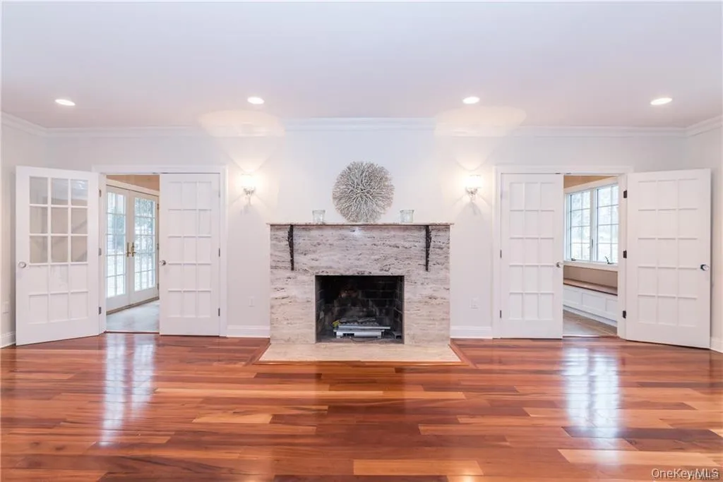 Unfurnished living room with french doors, crown molding, wood finished floors, a fireplace with flush hearth, and baseboards Unfurnished living room with french doors, crown molding, wood finished floors, a fireplace with flush hearth, and baseboards