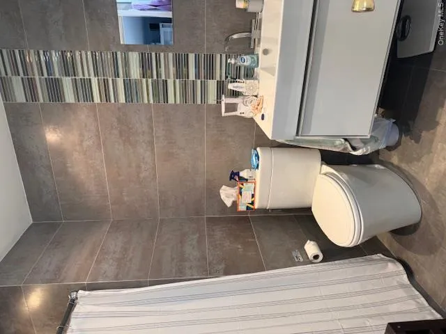 Bathroom with vanity, a shower with curtain, toilet, and tile walls Bathroom with vanity, a shower with curtain, toilet, and tile walls