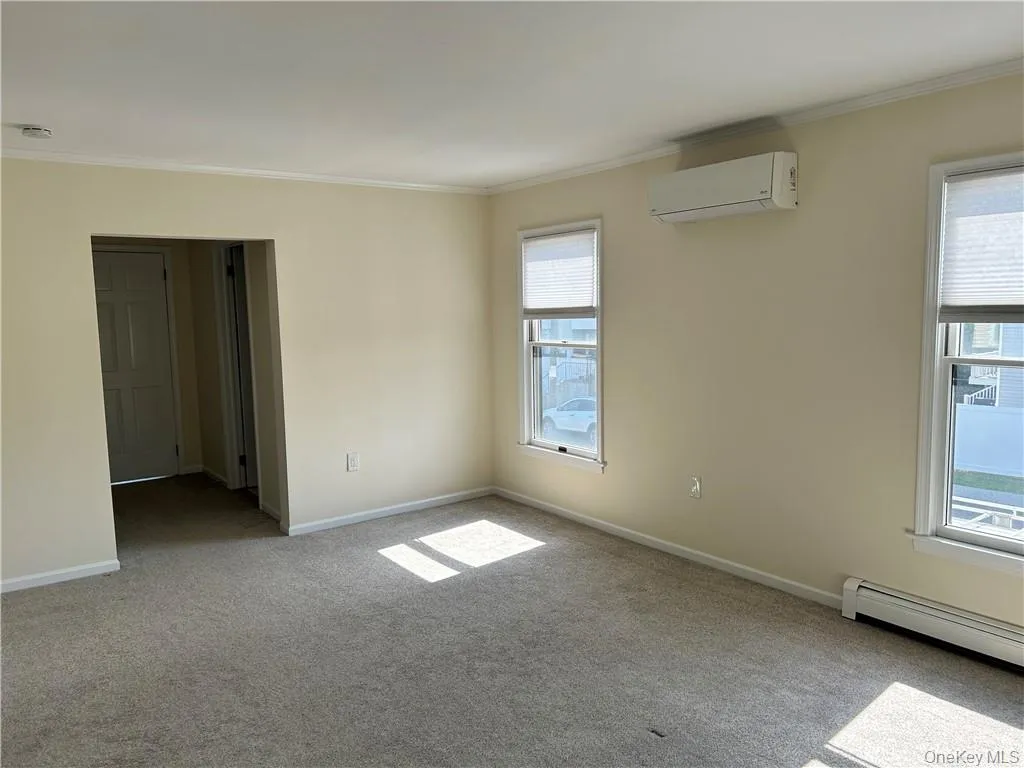 Empty room with a baseboard heating unit, ornamental molding, carpet floors, and a wall mounted air conditioner Empty room with a baseboard heating unit, ornamental molding, carpet floors, and a wall mounted air conditioner
