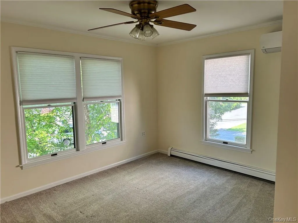 Carpeted spare room with crown molding, a baseboard radiator, ceiling fan, and an AC wall unit Carpeted spare room with crown molding, a baseboard radiator, ceiling fan, and an AC wall unit