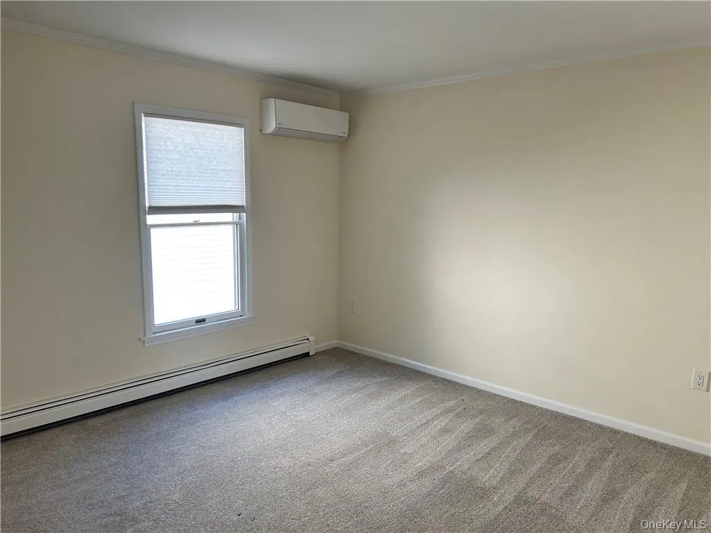 Empty room featuring a baseboard heating unit, ornamental molding, carpet floors, and a wall mounted AC Empty room featuring a baseboard heating unit, ornamental molding, carpet floors, and a wall mounted AC