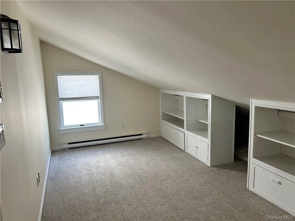Additional living space featuring a baseboard heating unit, vaulted ceiling, and light colored carpet Additional living space featuring a baseboard heating unit, vaulted ceiling, and light colored carpet