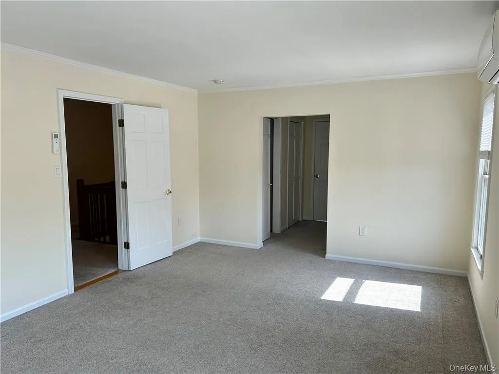 Empty room with crown molding, carpet floors, and an AC wall unit Empty room with crown molding, carpet floors, and an AC wall unit