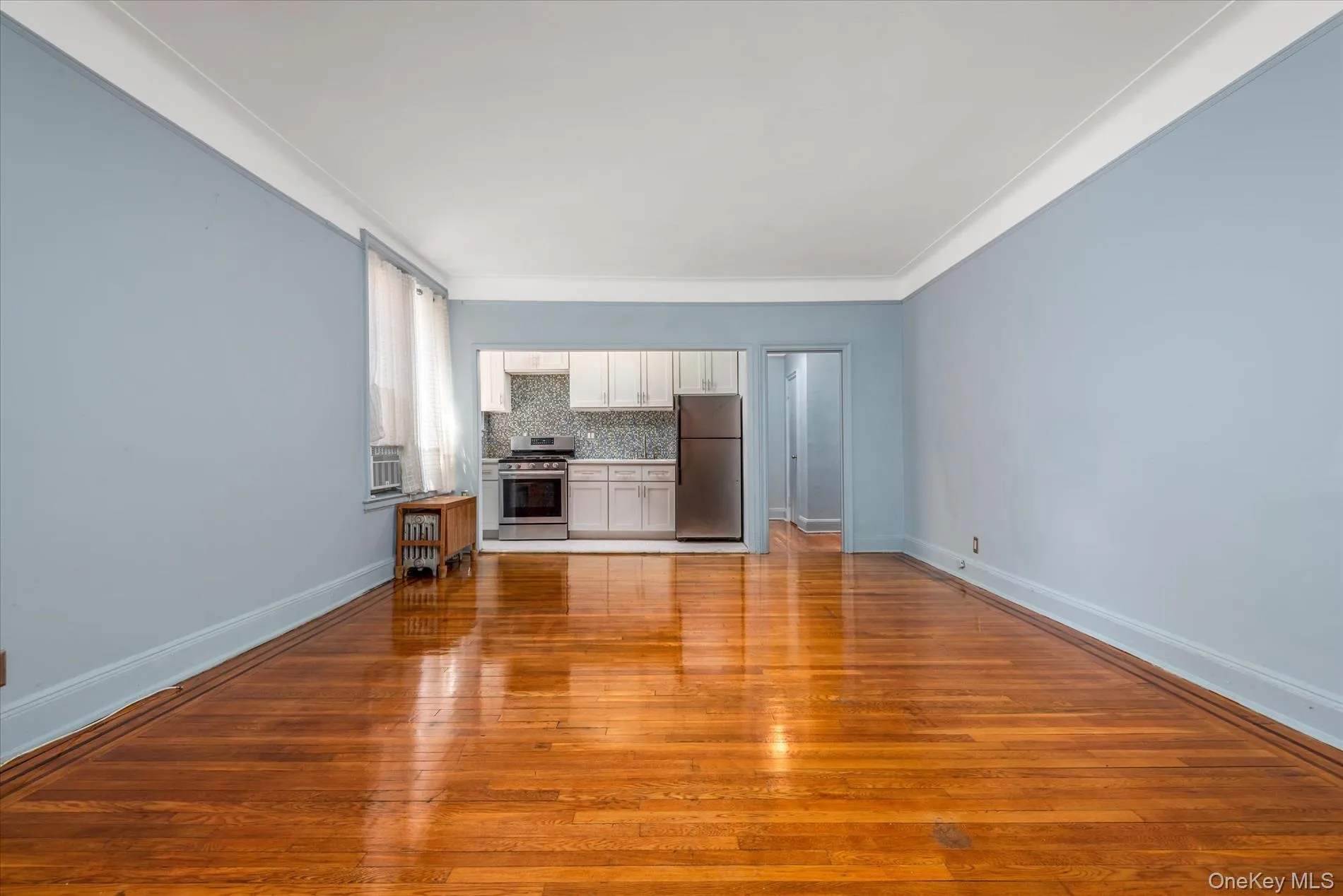 Hardwood flooring, crown molding, kitchen with stainless steel appliances, white cabinetry, and a patterned tile backsplash Hardwood flooring, crown molding, kitchen with stainless steel appliances, white cabinetry, and a patterned tile backsplash