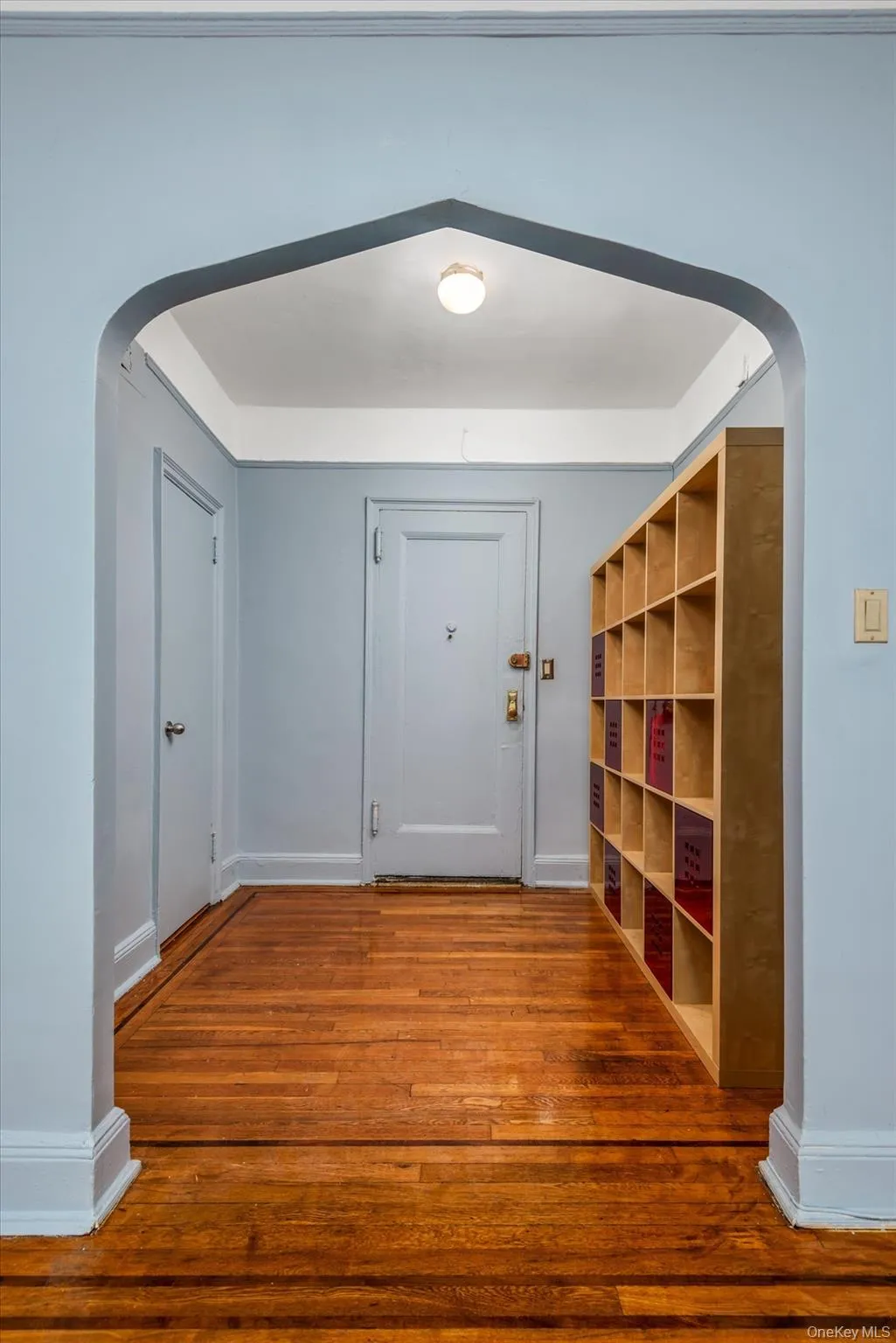 Bright hallway with recessed ceiling lighting, hardwood flooring throughout, and custom built-in wooden shelving with multiple compartments Bright hallway with recessed ceiling lighting, hardwood flooring throughout, and custom built-in wooden shelving with multiple compartments