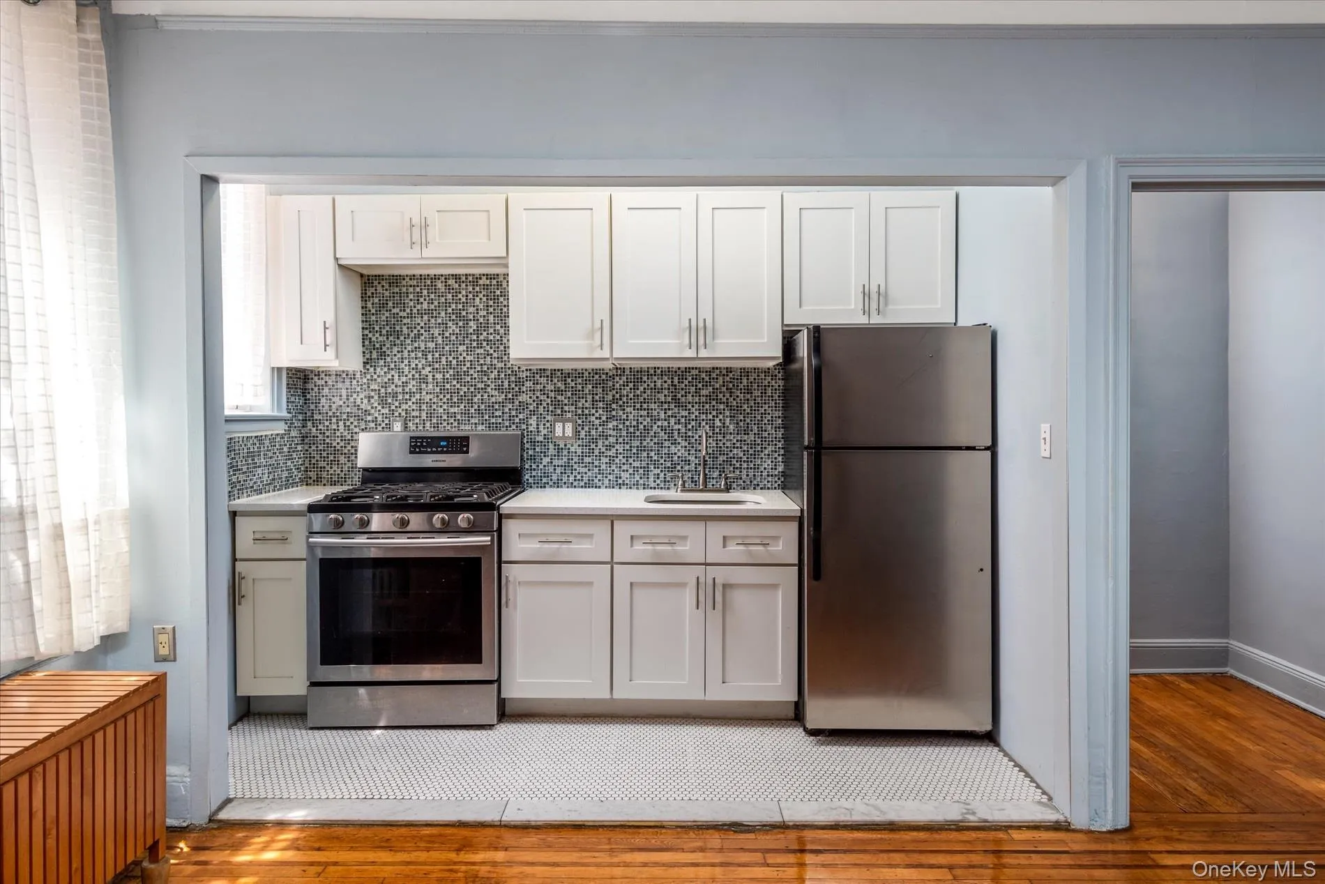 White shaker cabinetry, patterned backsplash, stainless steel appliances, white countertops, and tile flooring White shaker cabinetry, patterned backsplash, stainless steel appliances, white countertops, and tile flooring