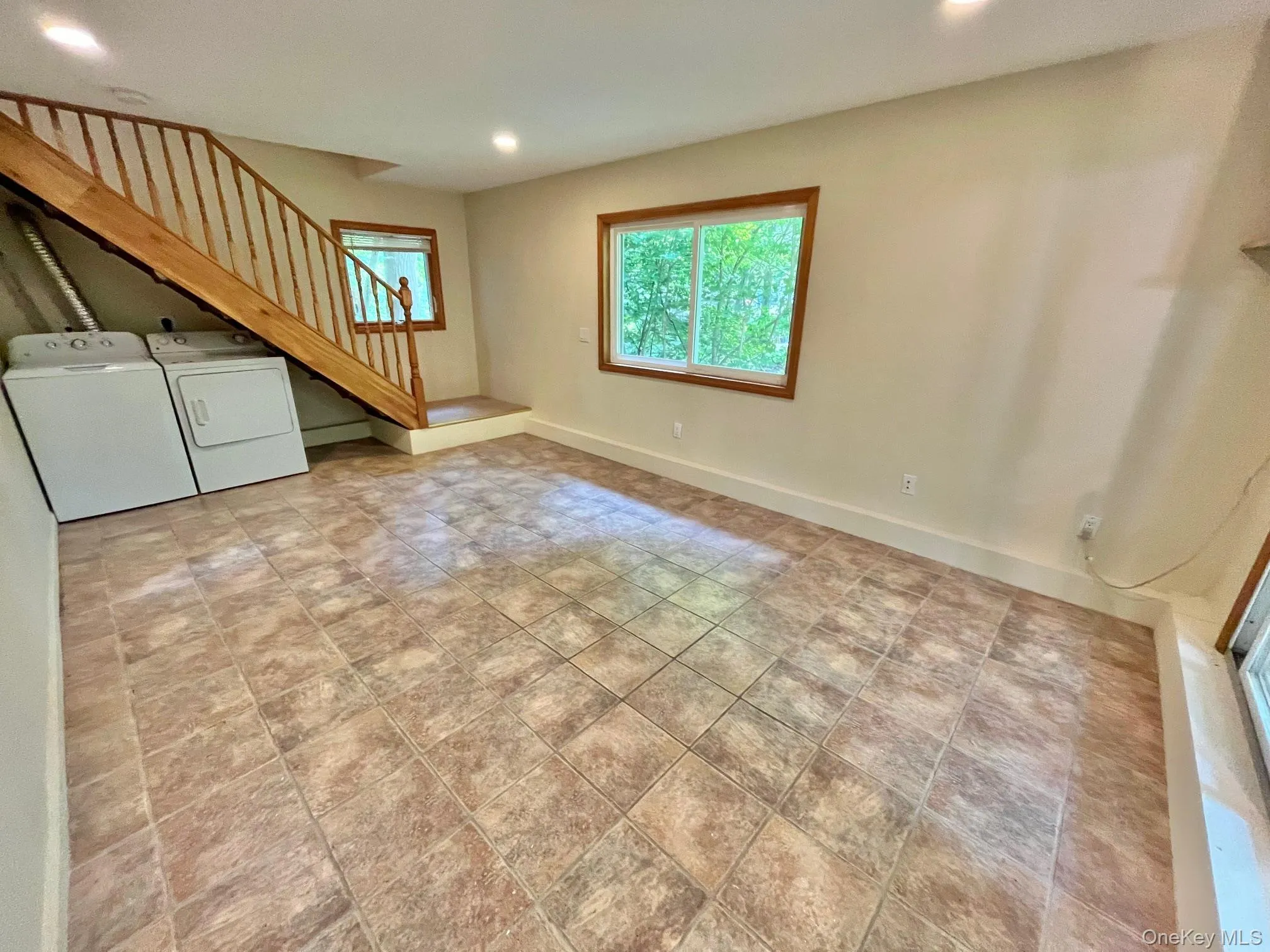 Unfurnished living room featuring washer and dryer, stairs, recessed lighting, baseboards, and stone finish flooring Unfurnished living room featuring washer and dryer, stairs, recessed lighting, baseboards, and stone finish flooring