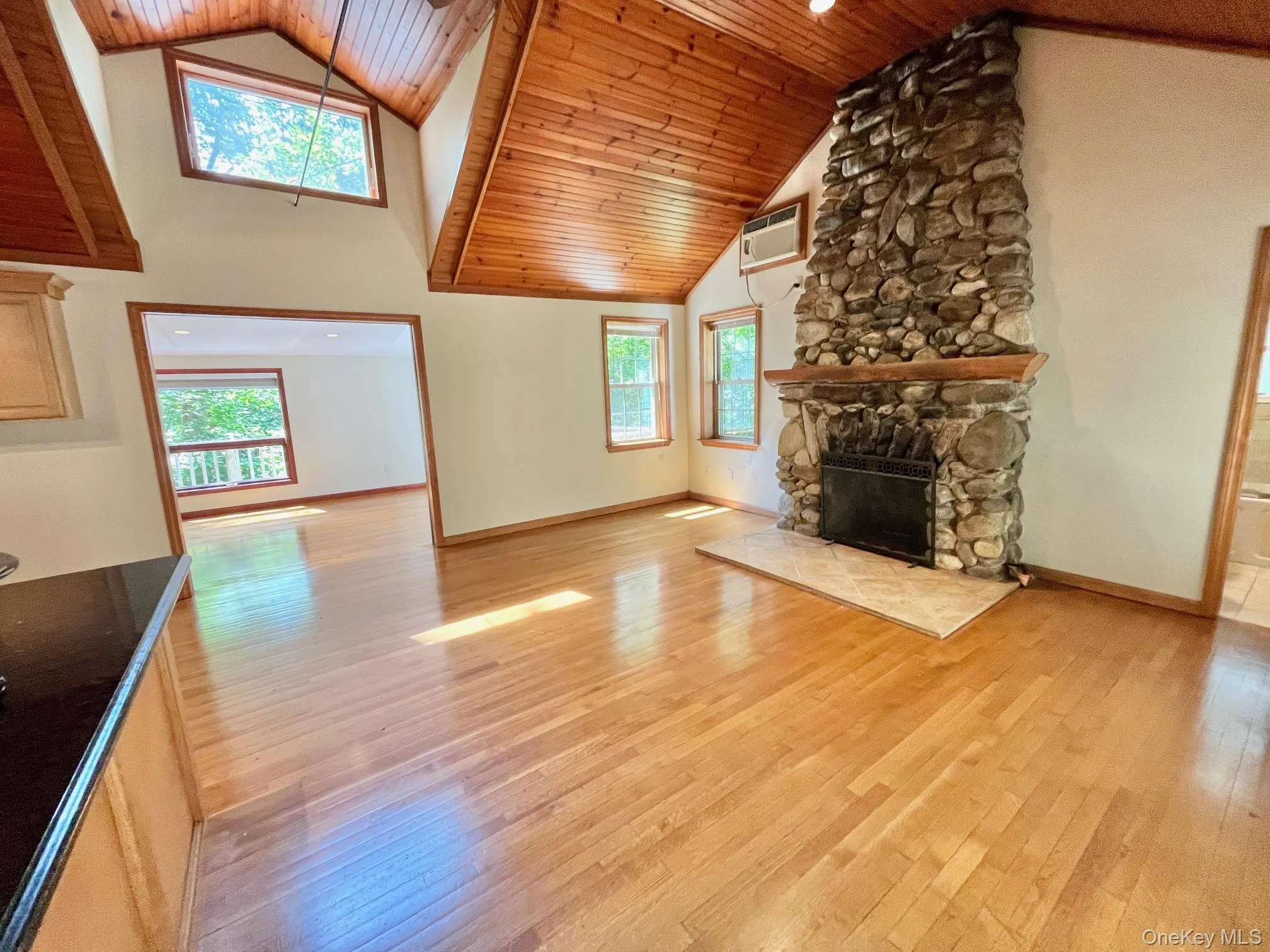 Unfurnished living room with high vaulted ceiling, light wood-style flooring, a stone fireplace, healthy amount of natural light, and wooden ceiling Unfurnished living room with high vaulted ceiling, light wood-style flooring, a stone fireplace, healthy amount of natural light, and wooden ceiling