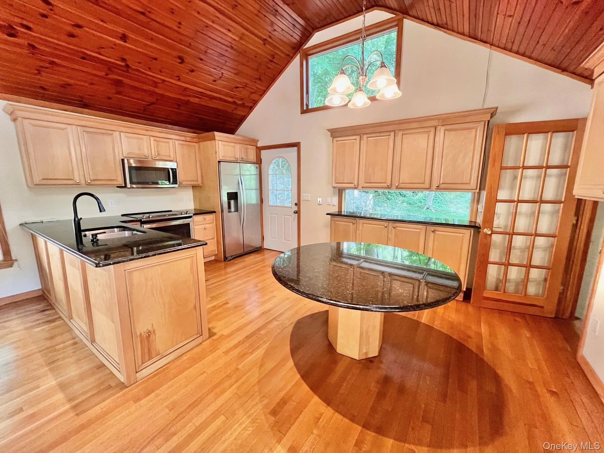 Kitchen featuring stainless steel appliances, a sink, a peninsula, light wood finished floors, and wood ceiling Kitchen featuring stainless steel appliances, a sink, a peninsula, light wood finished floors, and wood ceiling