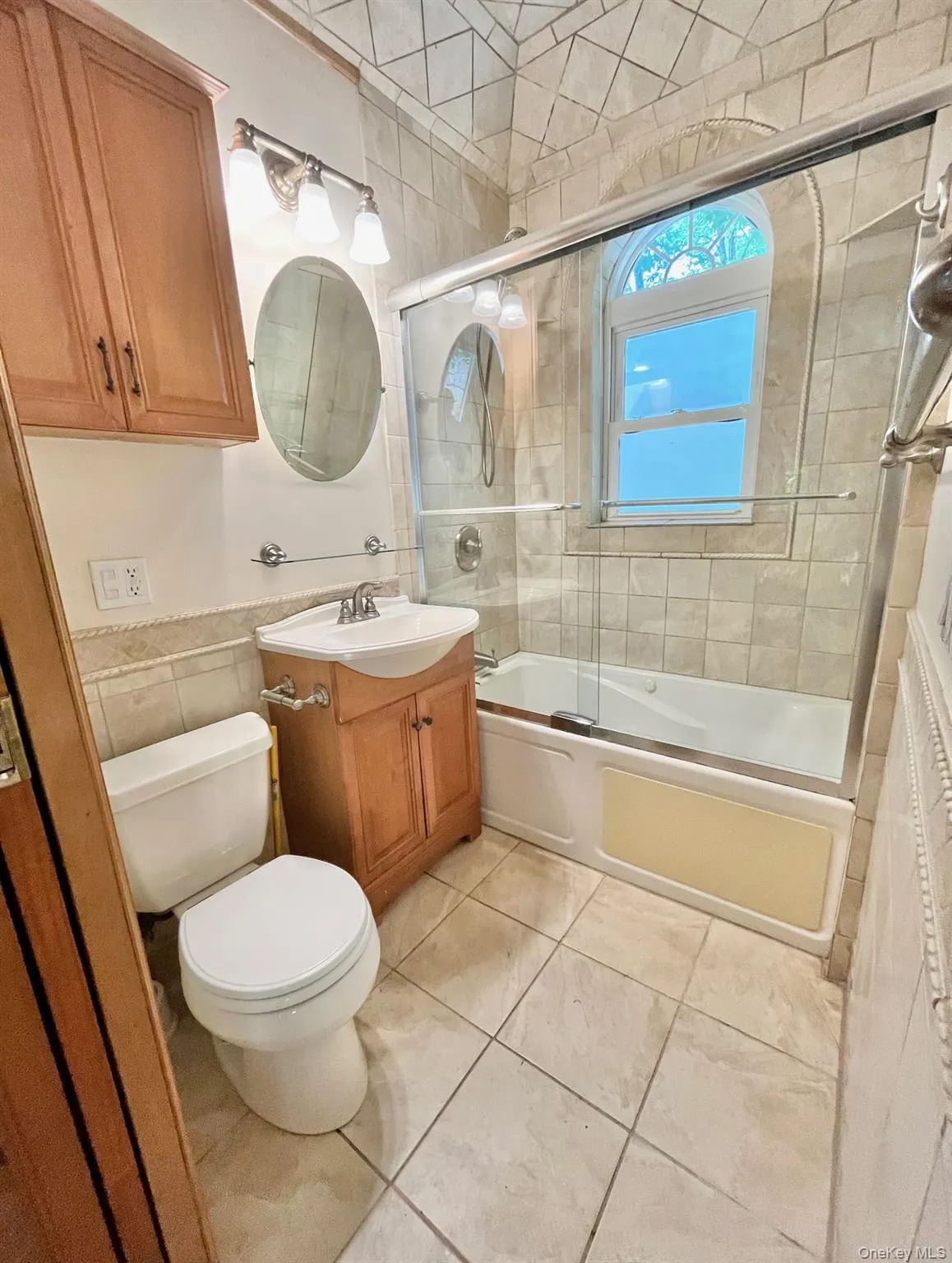 Full bath featuring vanity, bath / shower combo with glass door, toilet, tile walls, and tile patterned floors Full bath featuring vanity, bath / shower combo with glass door, toilet, tile walls, and tile patterned floors