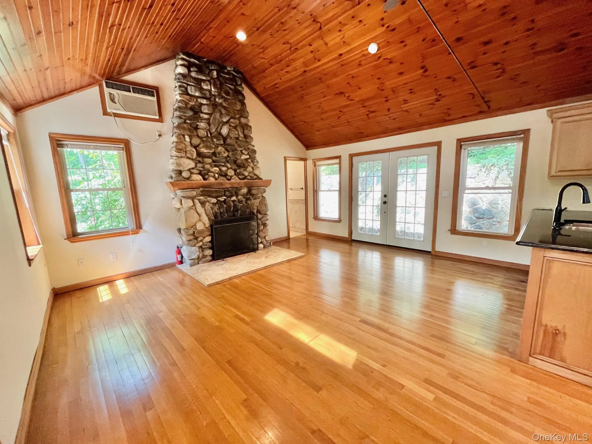 Unfurnished living room featuring a wall mounted air conditioner, baseboards, wooden ceiling, light wood-type flooring, and vaulted ceiling Unfurnished living room featuring a wall mounted air conditioner, baseboards, wooden ceiling, light wood-type flooring, and vaulted ceiling