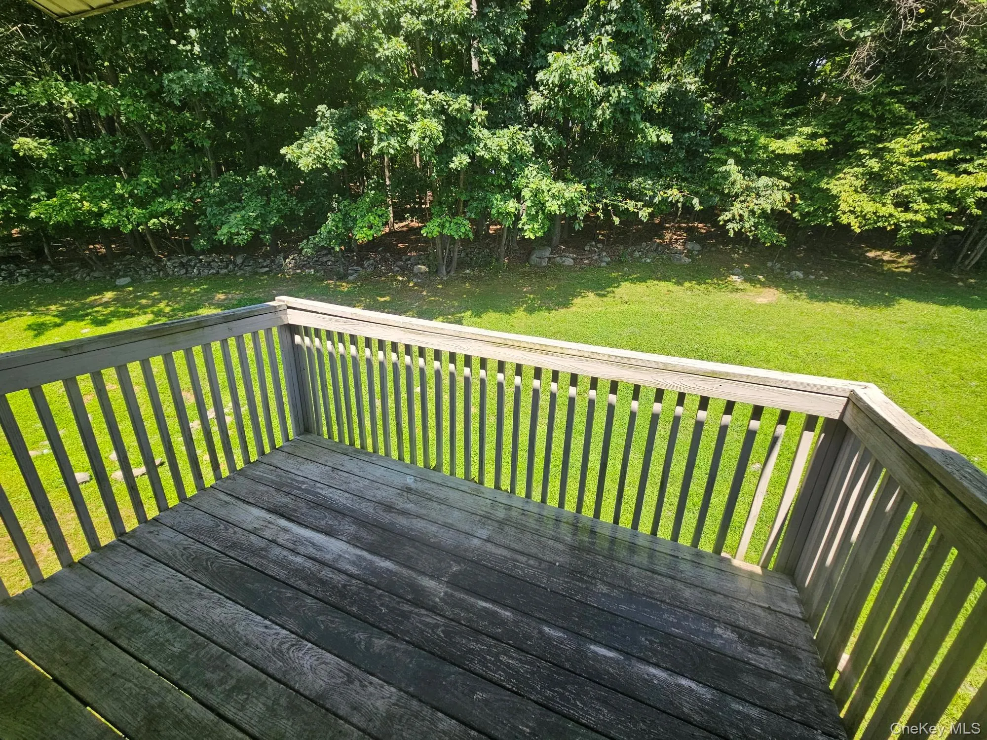 Wood-plank outdoor deck with wooden railing overlooking a green lawn and mature trees Wood-plank outdoor deck with wooden railing overlooking a green lawn and mature trees