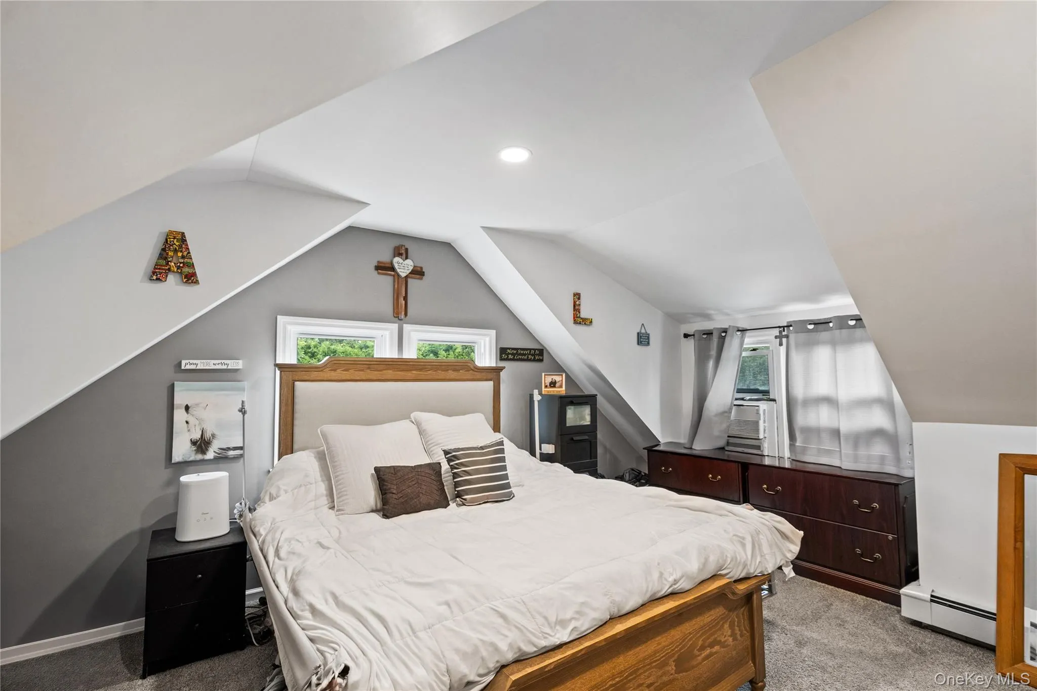 Bedroom featuring light colored carpet, a baseboard heating unit, lofted ceiling, and multiple windows Bedroom featuring light colored carpet, a baseboard heating unit, lofted ceiling, and multiple windows