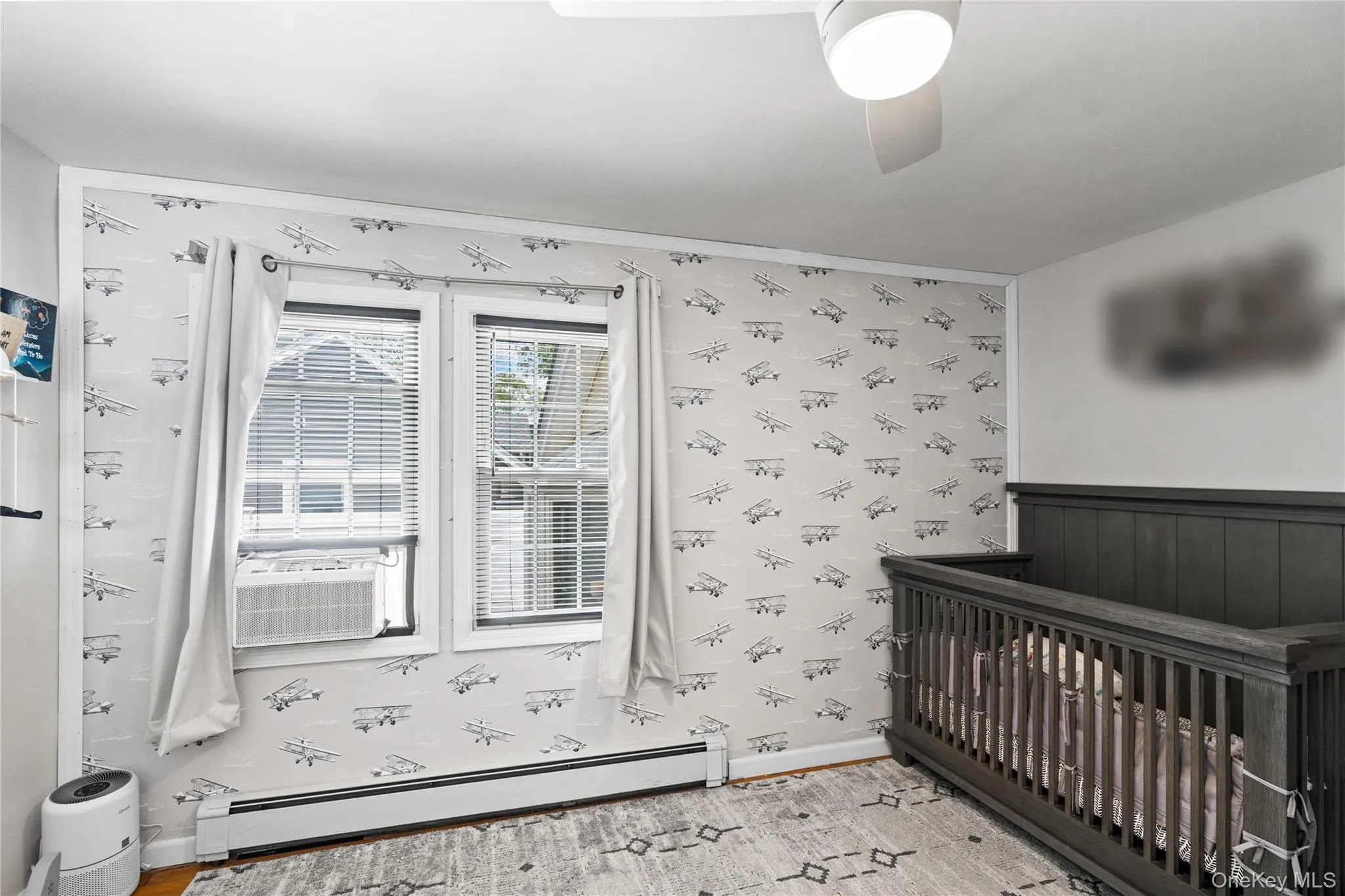 Unfurnished bedroom with a baseboard radiator, wallpapered walls, light wood-style flooring, cooling unit, and baseboards Unfurnished bedroom with a baseboard radiator, wallpapered walls, light wood-style flooring, cooling unit, and baseboards