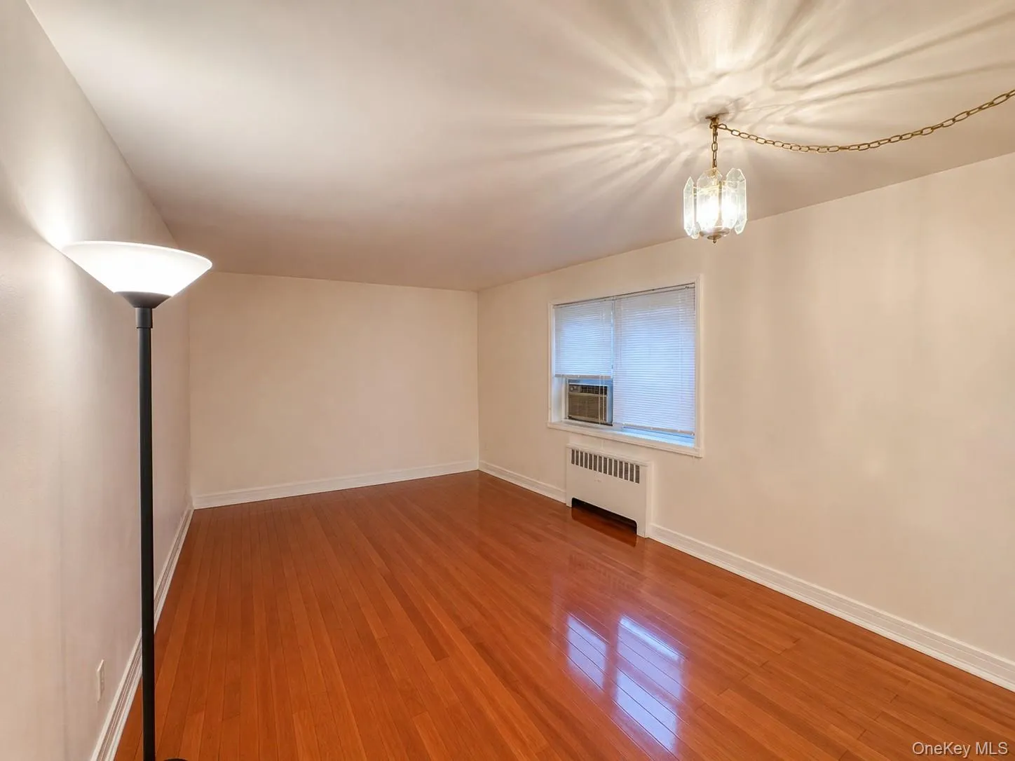 Living room with a large window, wood floors, and radiator heat. Living room with a large window, wood floors, and radiator heat.
