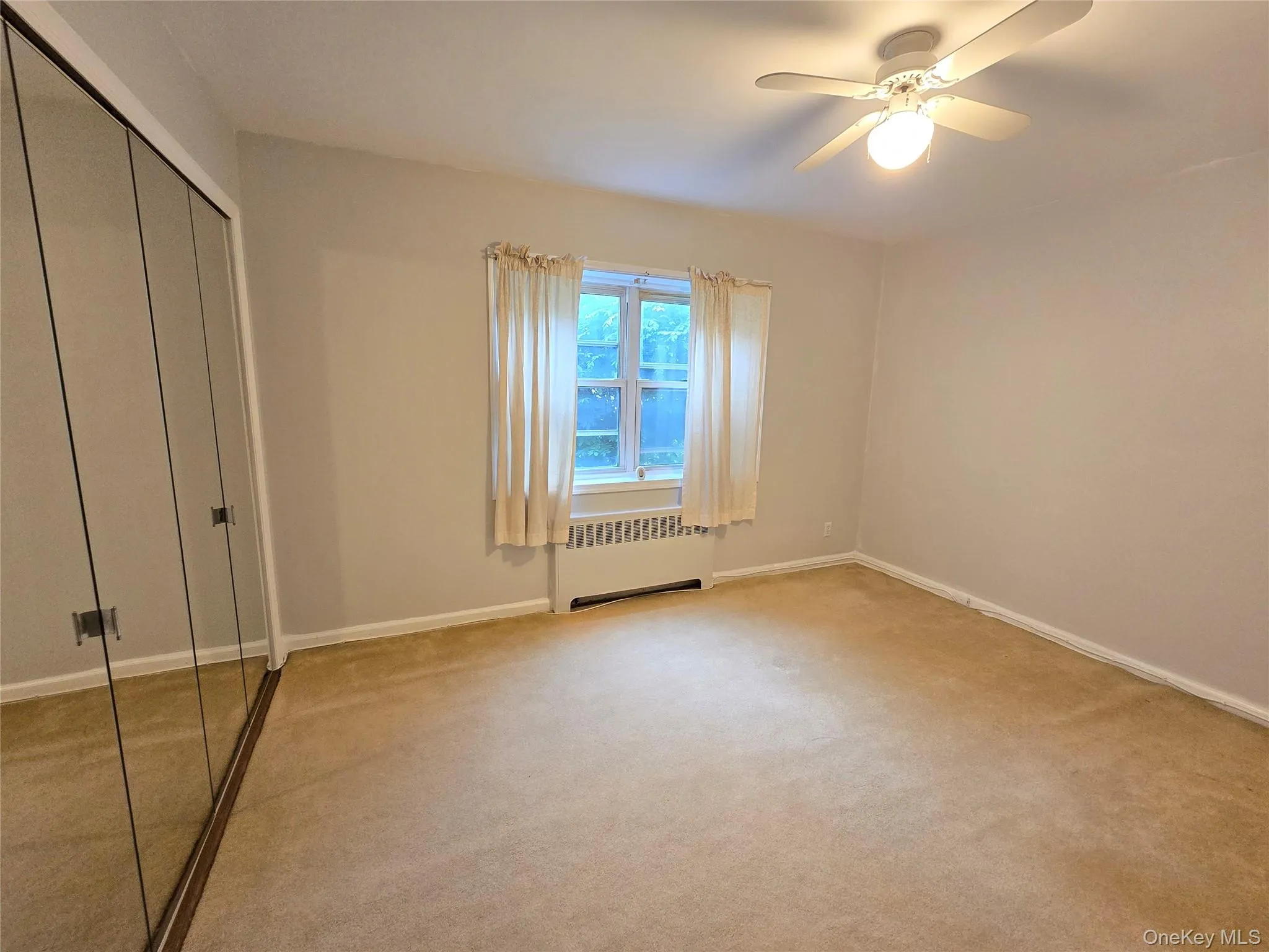 Bright bedroom with mirrored closet, ceiling fan, and window. Bright bedroom with mirrored closet, ceiling fan, and window.