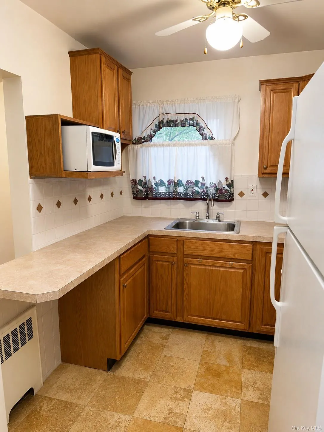 Windowed kitchen with full-size refrigerator, gas range, oak cabinetry, and tile backsplash. Windowed kitchen with full-size refrigerator, gas range, oak cabinetry, and tile backsplash.