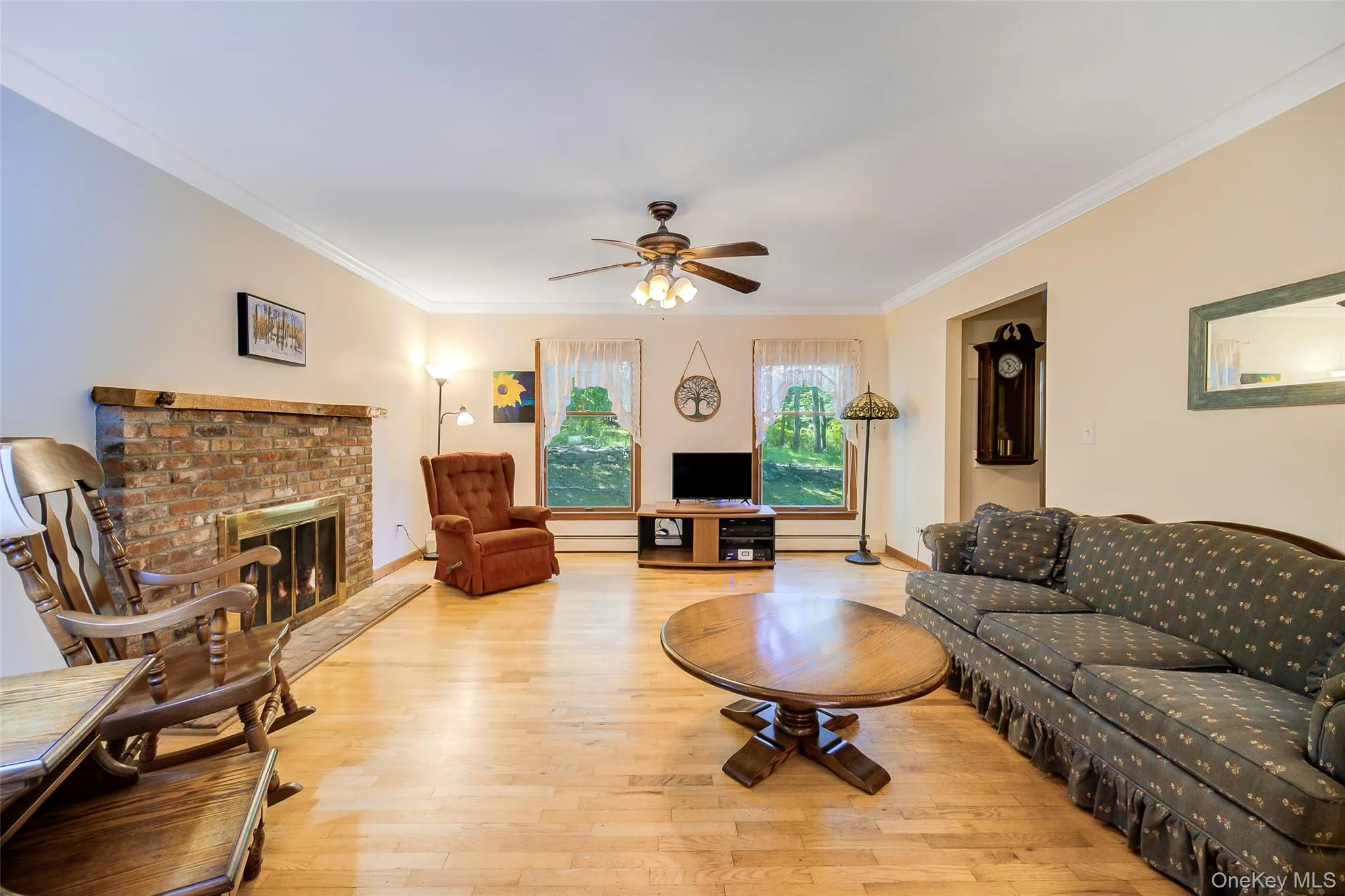Hardwood flooring, brick fireplace with wood mantel, crown molding, ceiling fan, and large windows Hardwood flooring, brick fireplace with wood mantel, crown molding, ceiling fan, and large windows