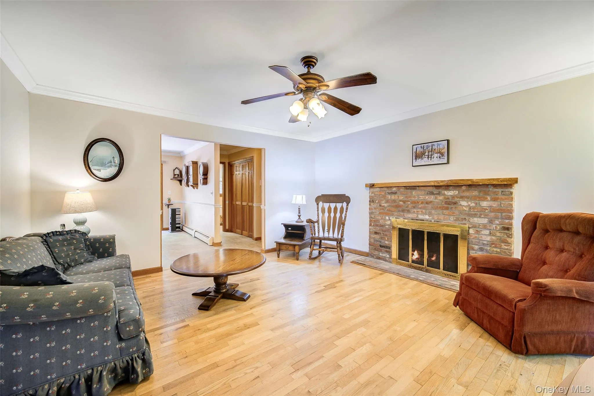 Hardwood flooring, crown molding, brick fireplace with a wood mantle, and a ceiling fan with integrated lighting Hardwood flooring, crown molding, brick fireplace with a wood mantle, and a ceiling fan with integrated lighting