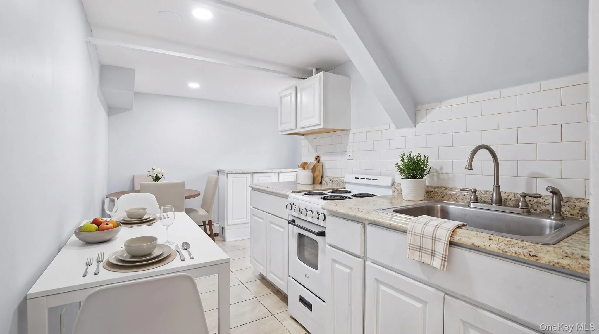 White subway tile backsplash, white cabinetry, granite-style countertop, stainless steel sink, and tile flooring White subway tile backsplash, white cabinetry, granite-style countertop, stainless steel sink, and tile flooring