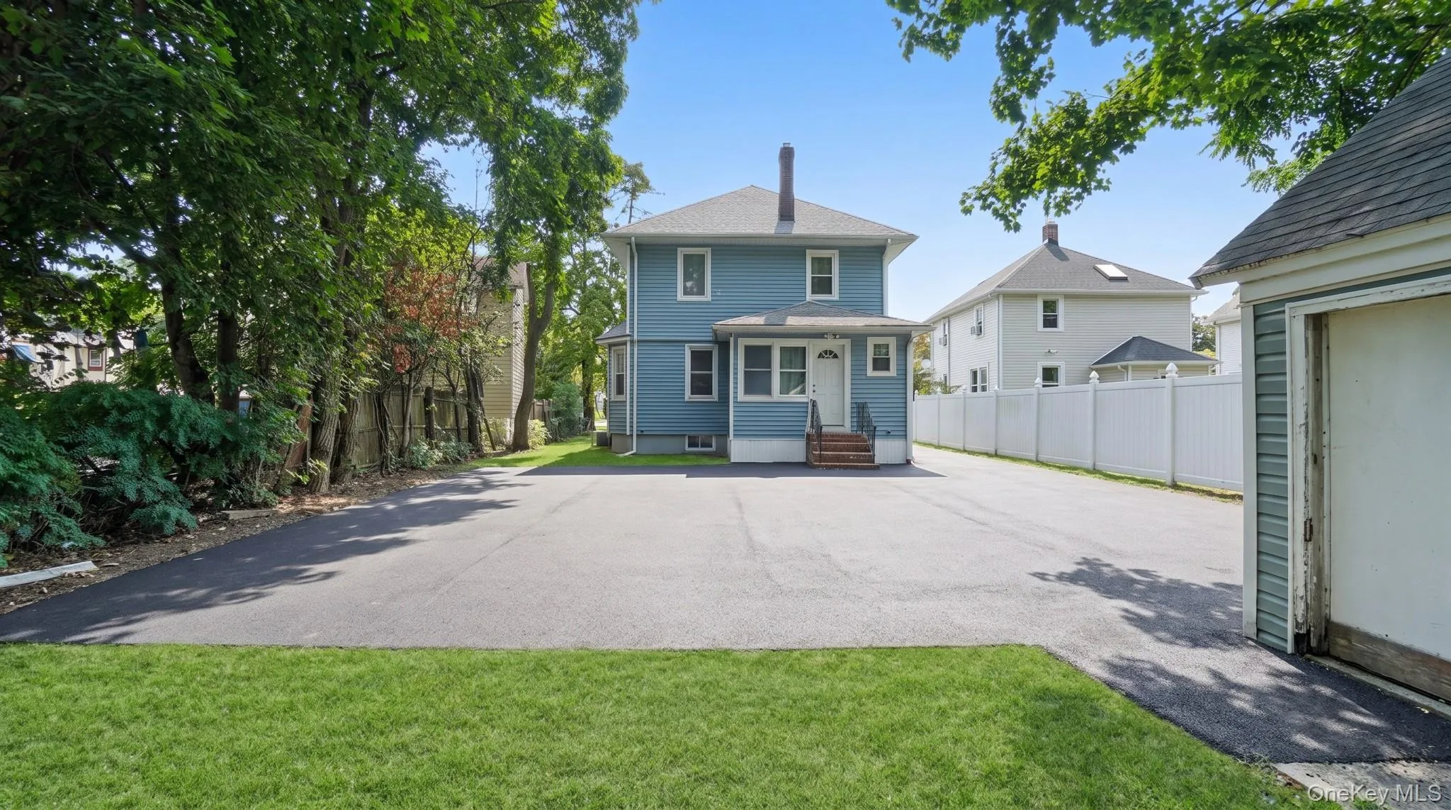 Expansive asphalt driveway with a detached garage and a privacy fence Expansive asphalt driveway with a detached garage and a privacy fence